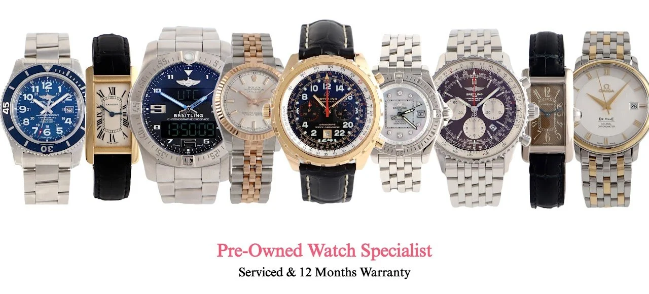 Pre-owned luxury watches displayed in a showroom, featuring stainless steel and gold timepieces by Rolex, Cartier, Omega, Breitling