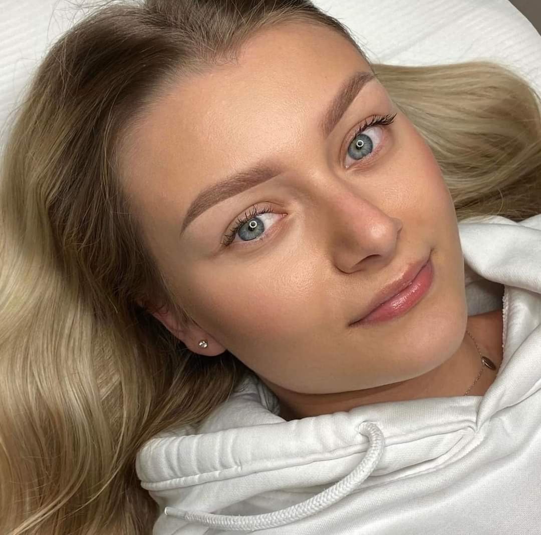 Nærbilde av en smilende kvinne med blondt hår og blå øyne, iført hvit hettegenser.