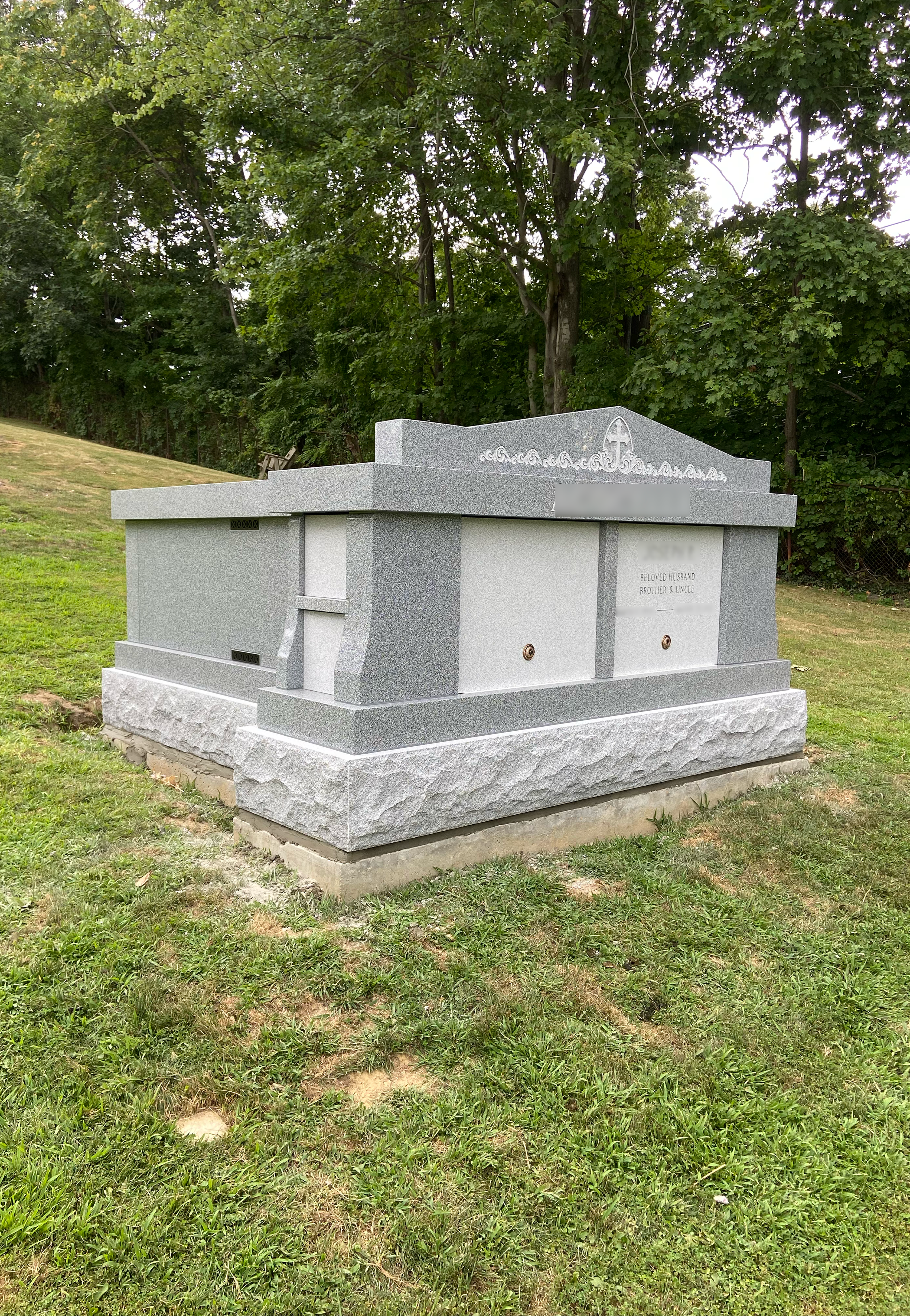 A gray granite mausoleum in a grassy cemetery, surrounded by trees.
