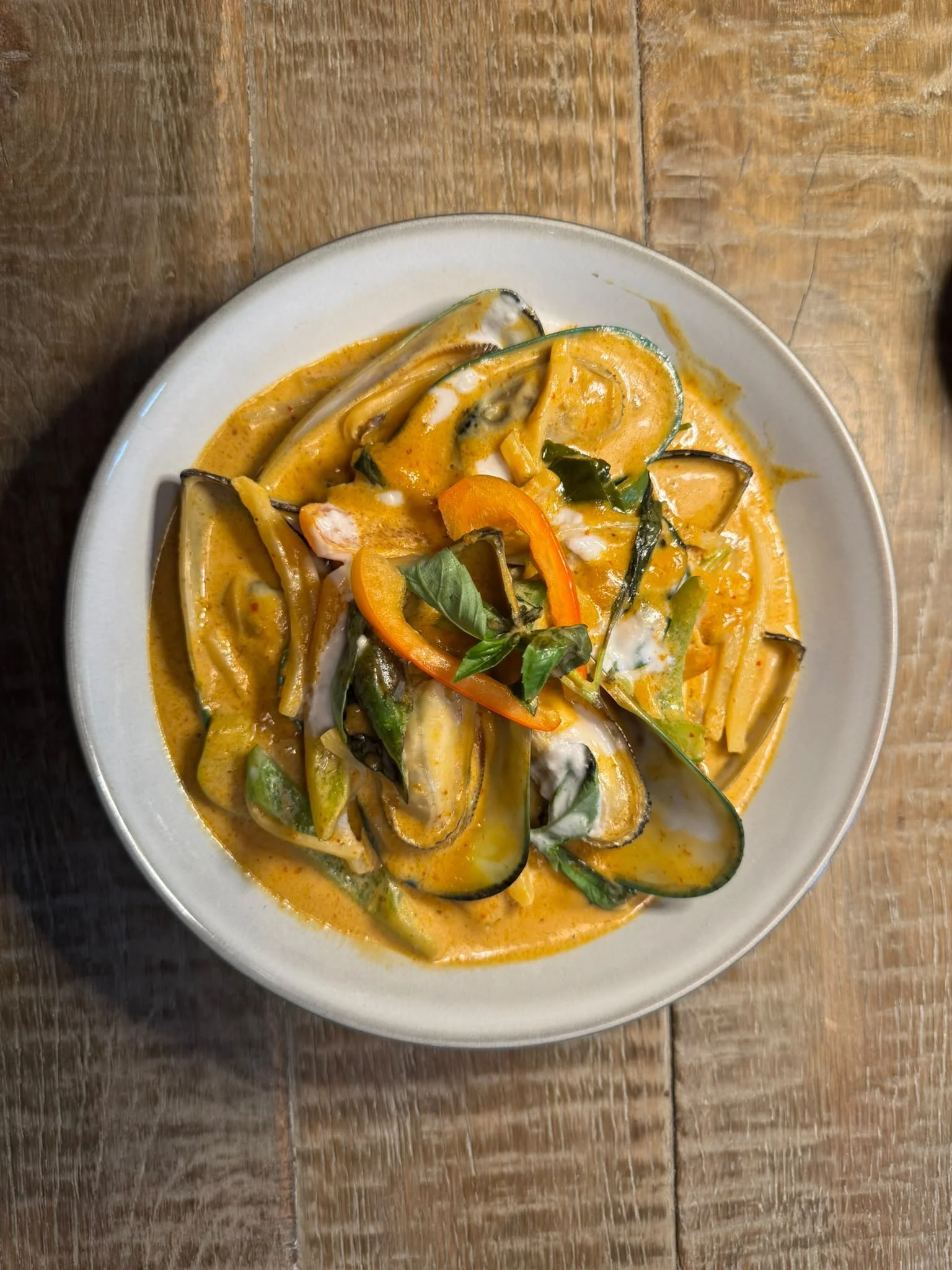 A white bowl of yellow curry with green, red, and purple vegetables, served on a wooden table.