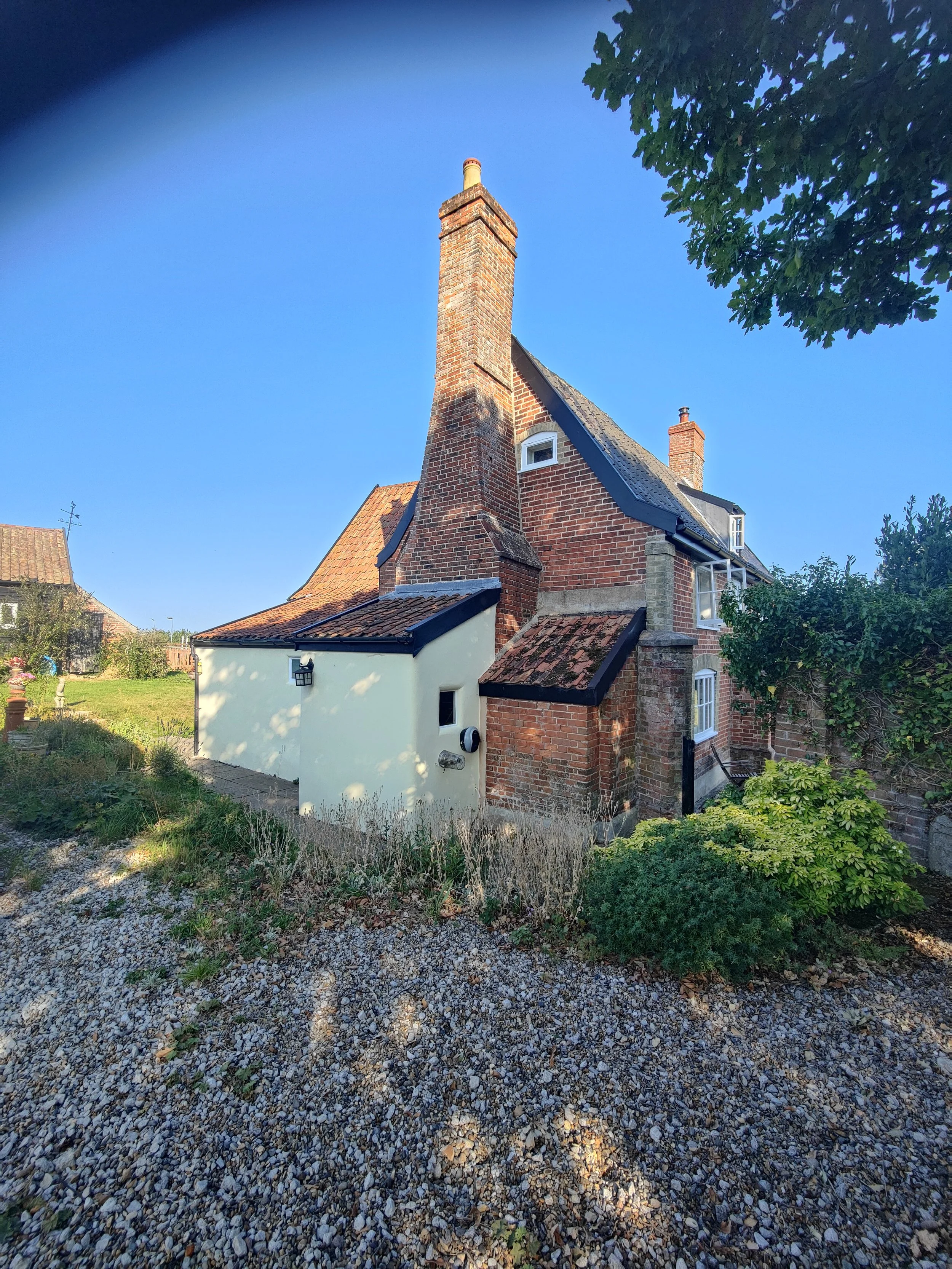 A brick house with a tall chimney, blue sky, and trees around