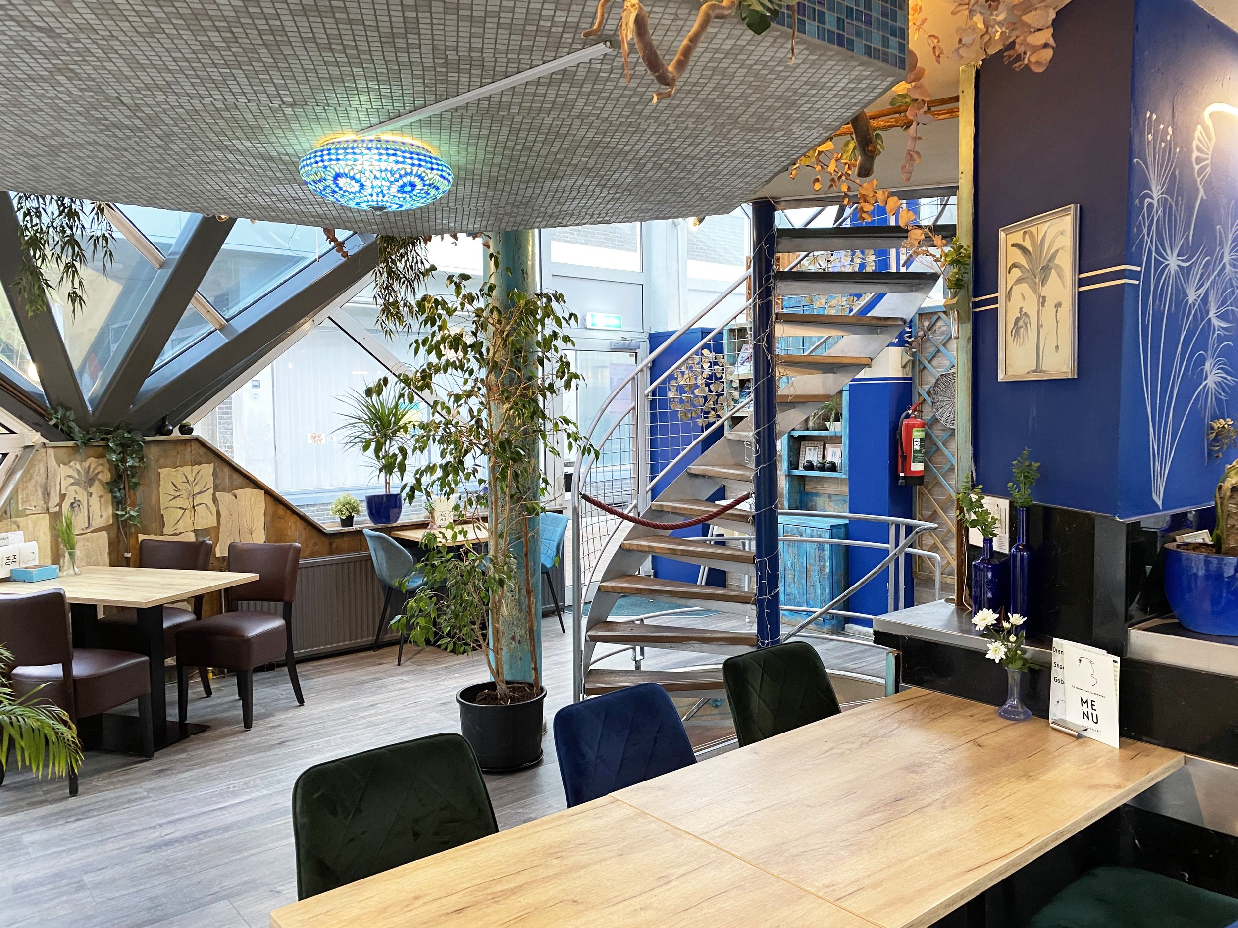 Het sfeervolle interieur van De Serre van Cleopatra in Wageningen, met houten tafels en blauwe accenten.