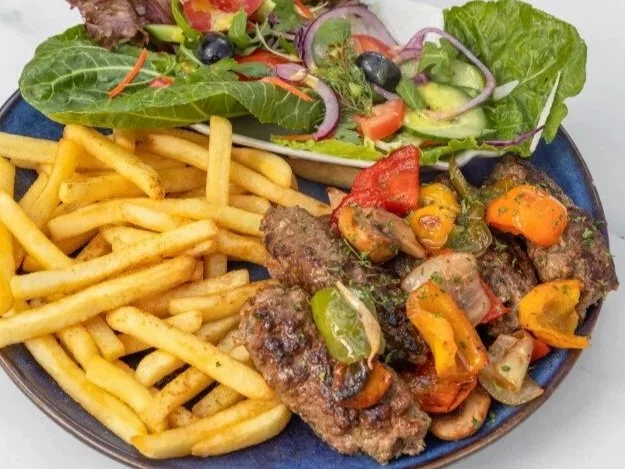 Bord met friet, gegrild vlees met paprika en tomaat, en een frisse groene salade