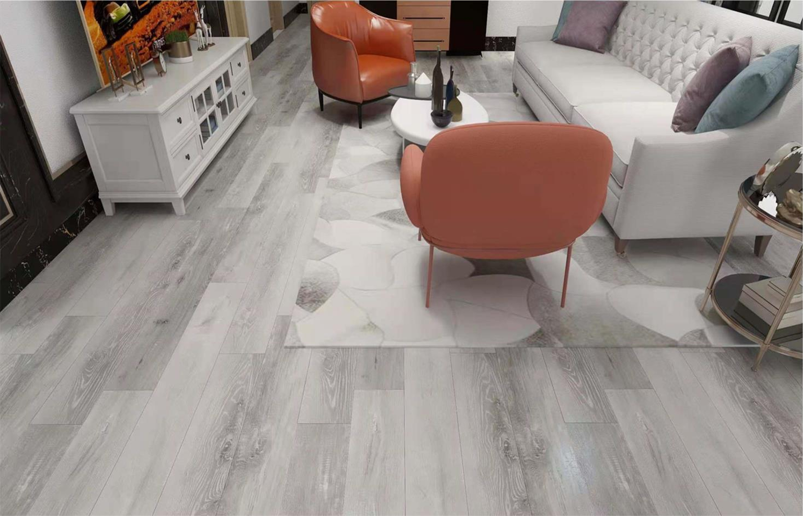 Living room with white tufted sofa, two coral armchairs, a round white coffee table with vases, and a white and gold side table, all on a light gray and white abstract-patterned rug and gray wood flooring.