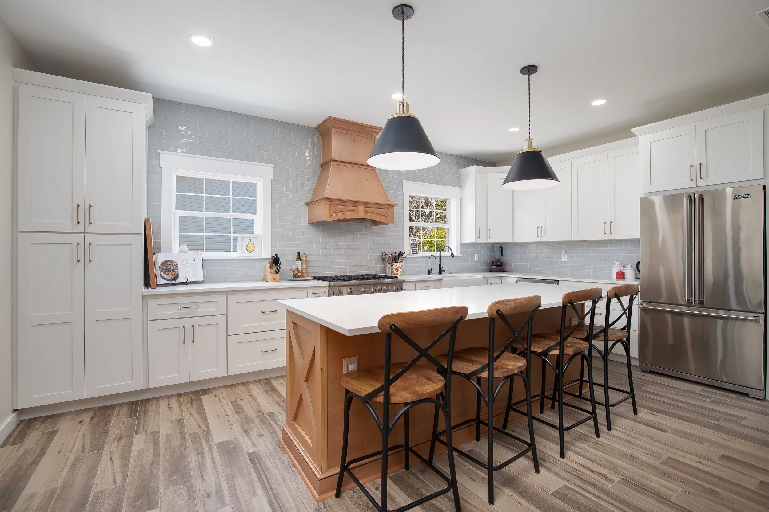 Bright kitchen featuring white cabinetry, a large wooden range hood, and a central island with bar stools.