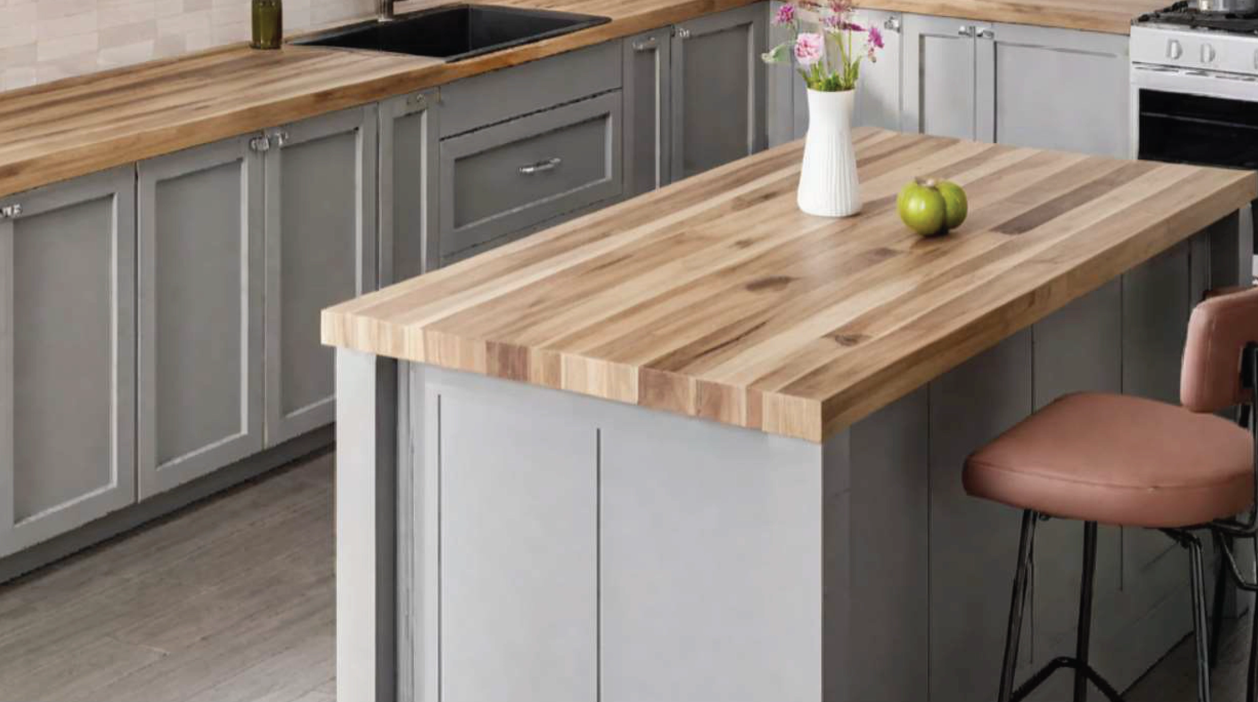 Grey kitchen island featuring Acacia countertop, two green apples and a vase with flowers.