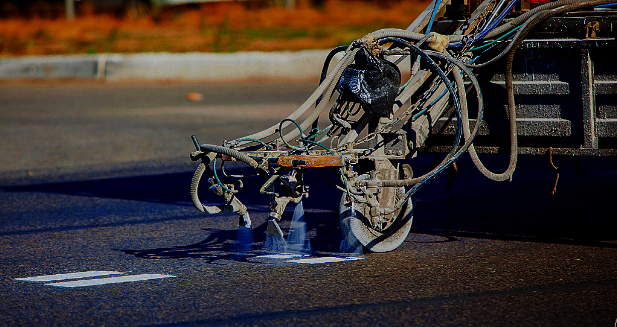 Asphalt paving machine laying fresh blacktop on a road surface with a blurred background of trees and sky.