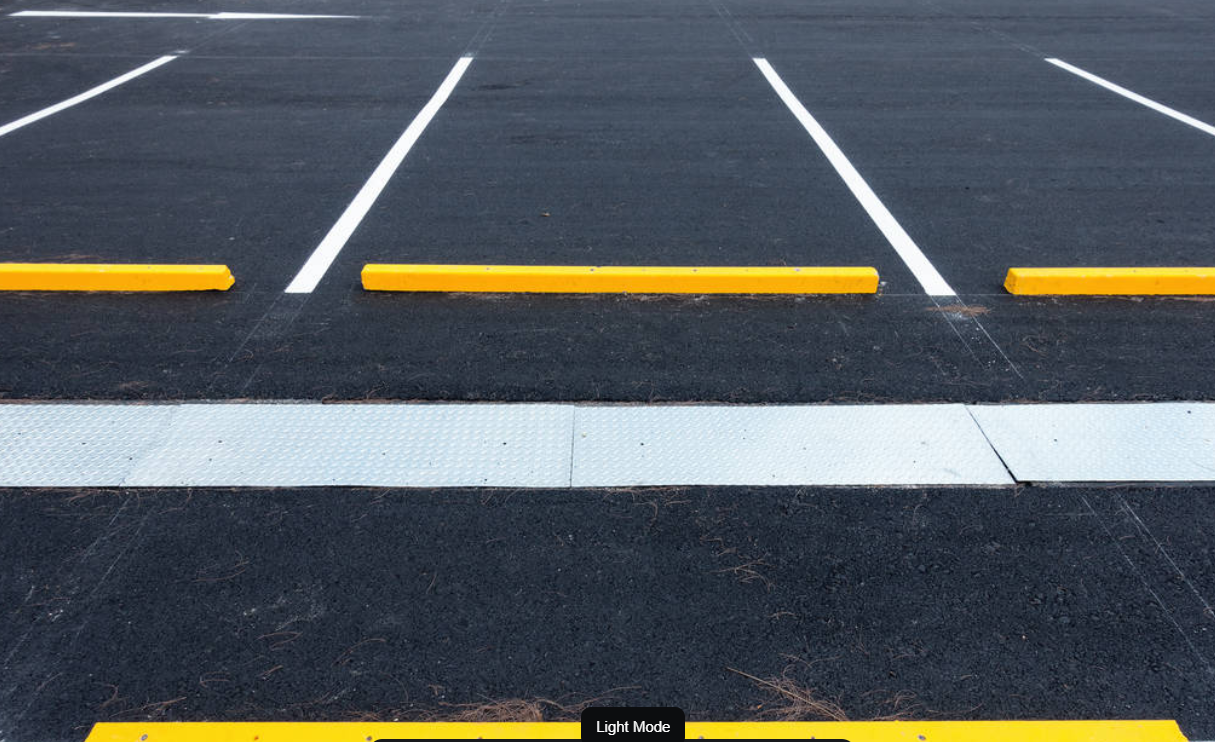 Empty parking lot with white parking lines, yellow parking barriers, and a white pedestrian crossing on asphalt.