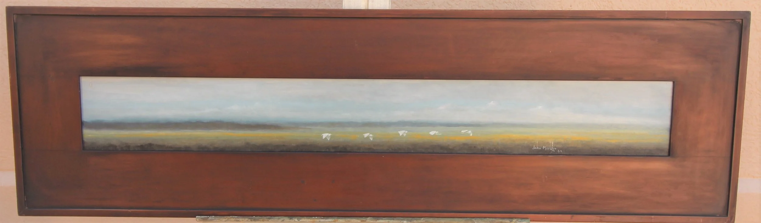 A horizontal landscape painting in a wooden frame, featuring a vast, open field with a few white birds flying in the distance under a cloudy sky.