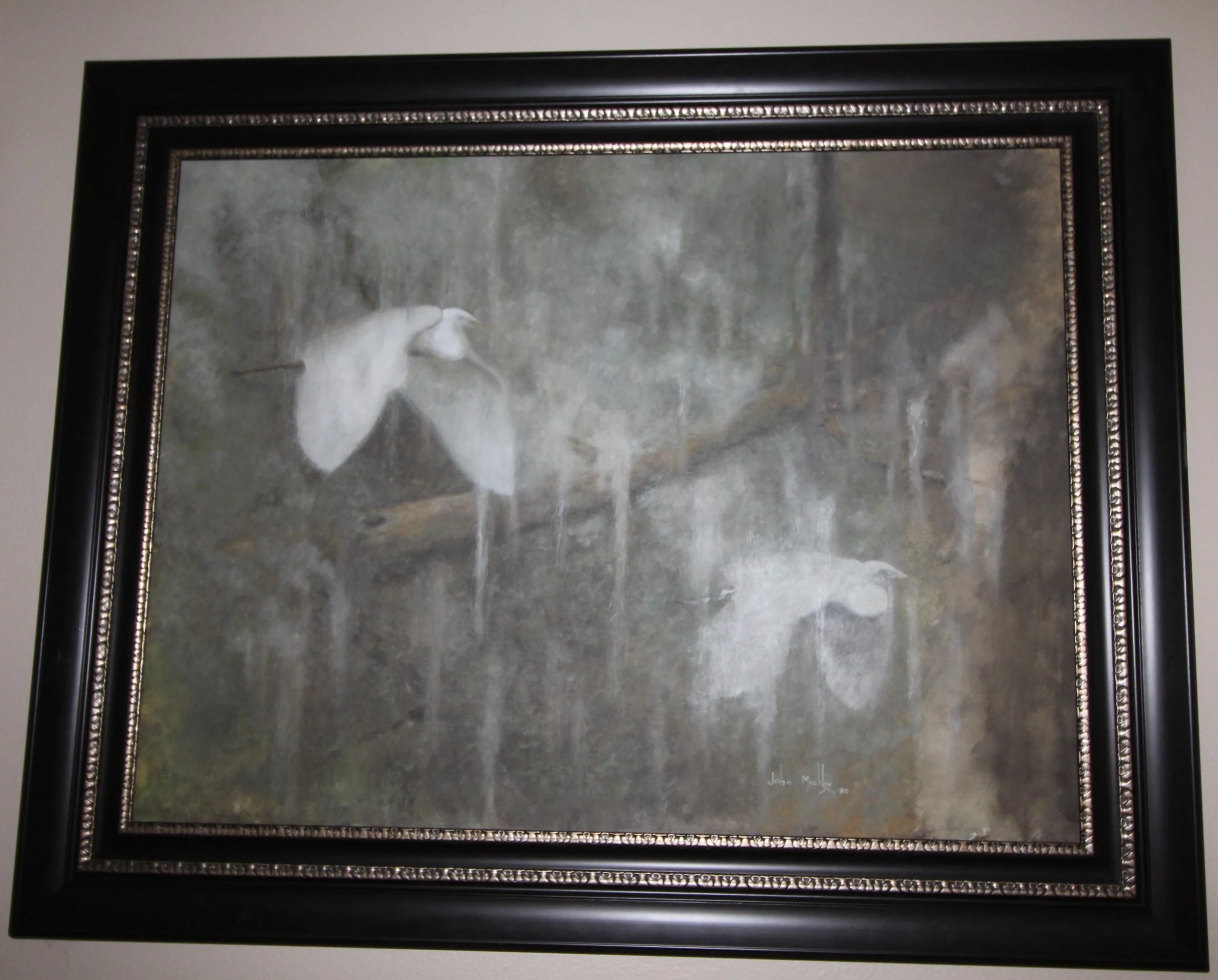 Painting of two white herons standing in a natural setting with trees in the background, framed in a black ornate frame.