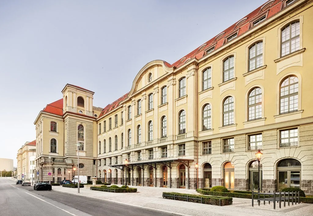 Historisches mehrstöckiges Gebäude mit gelben Wänden, roten Ziegeldächern und großen Fenstern, entlang einer ruhigen Straße mit Laternen und einigen Autos in Berlin.