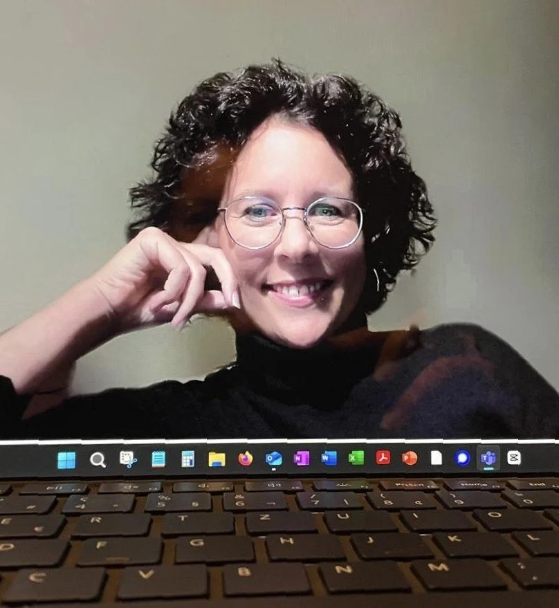 Ein Laptop-Bildschirm zeigt ein lachendes Gesicht einer Frau mit Brille, die auf einem Stuhl sitzt.