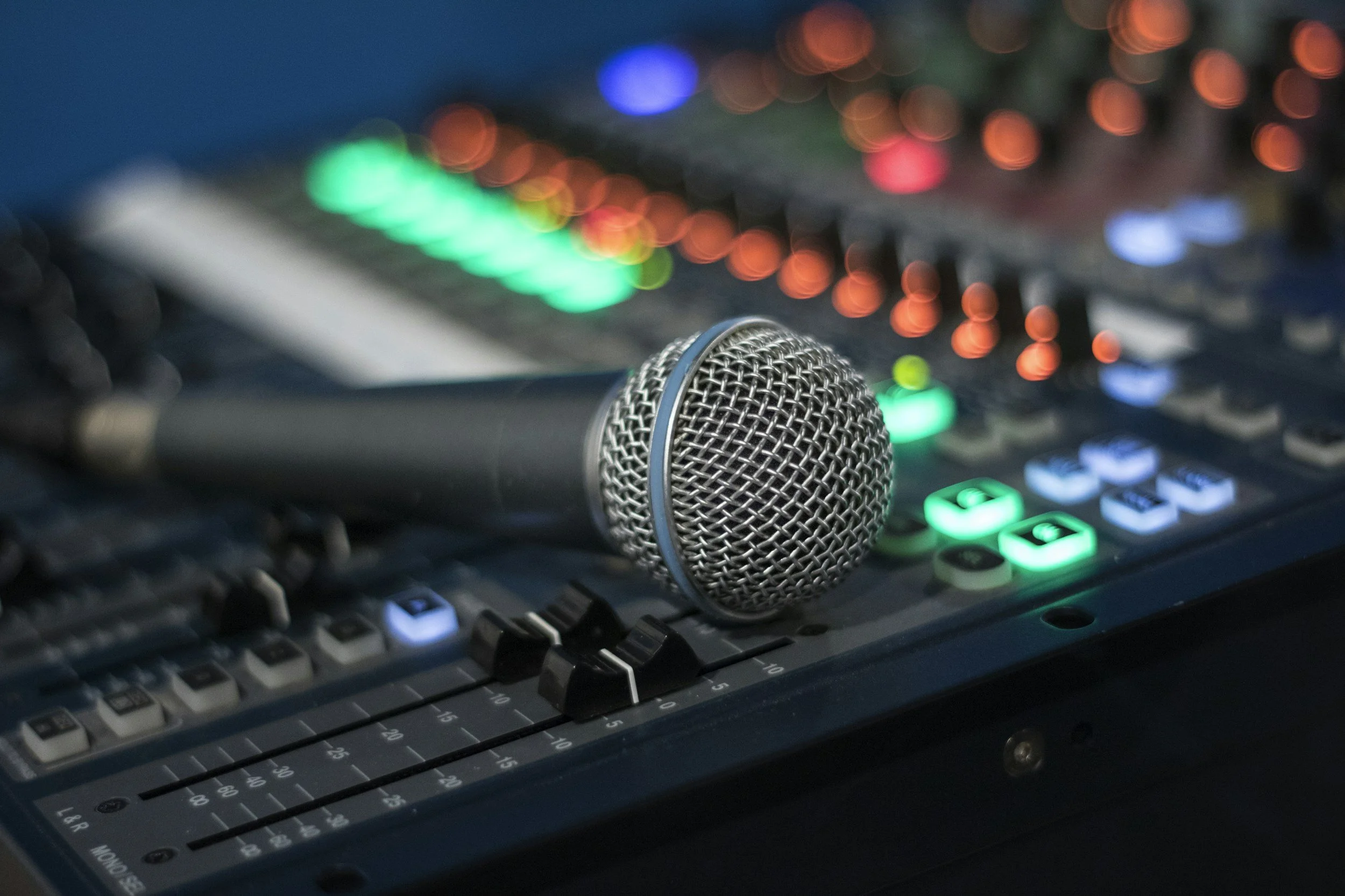 A microphone resting on a DJ mixing console with colorful illuminated controls.