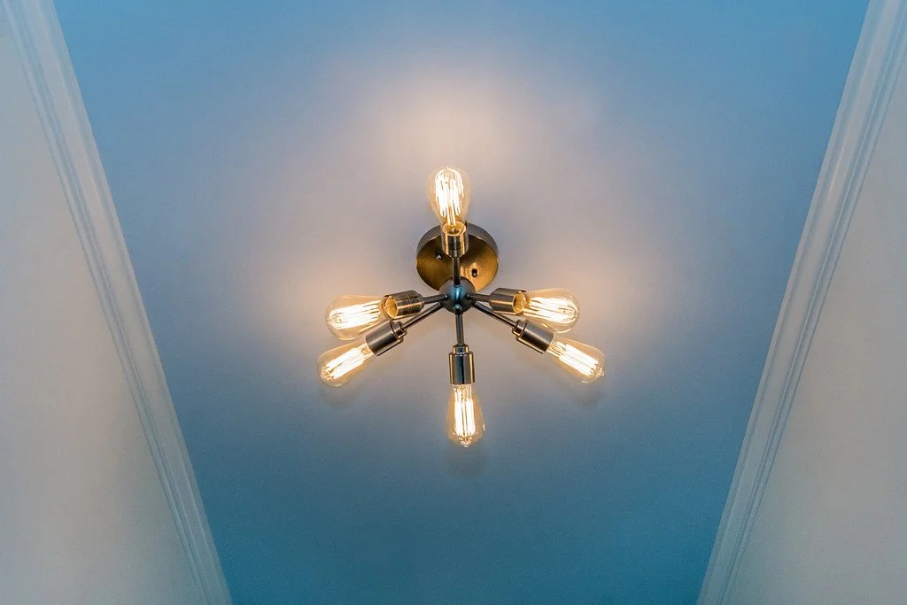 Ceiling light fixture with five exposed bulbs mounted on a brass base against a light blue ceiling.