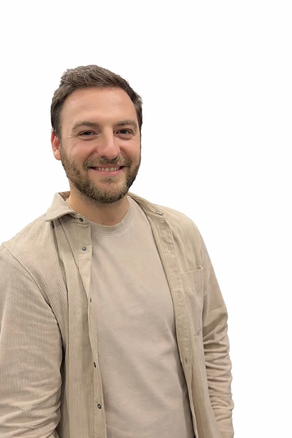 Een lachende man met een baard en kort bruin haar draagt een beige shirt en een lichtbruin vest, staand voor een witte achtergrond.