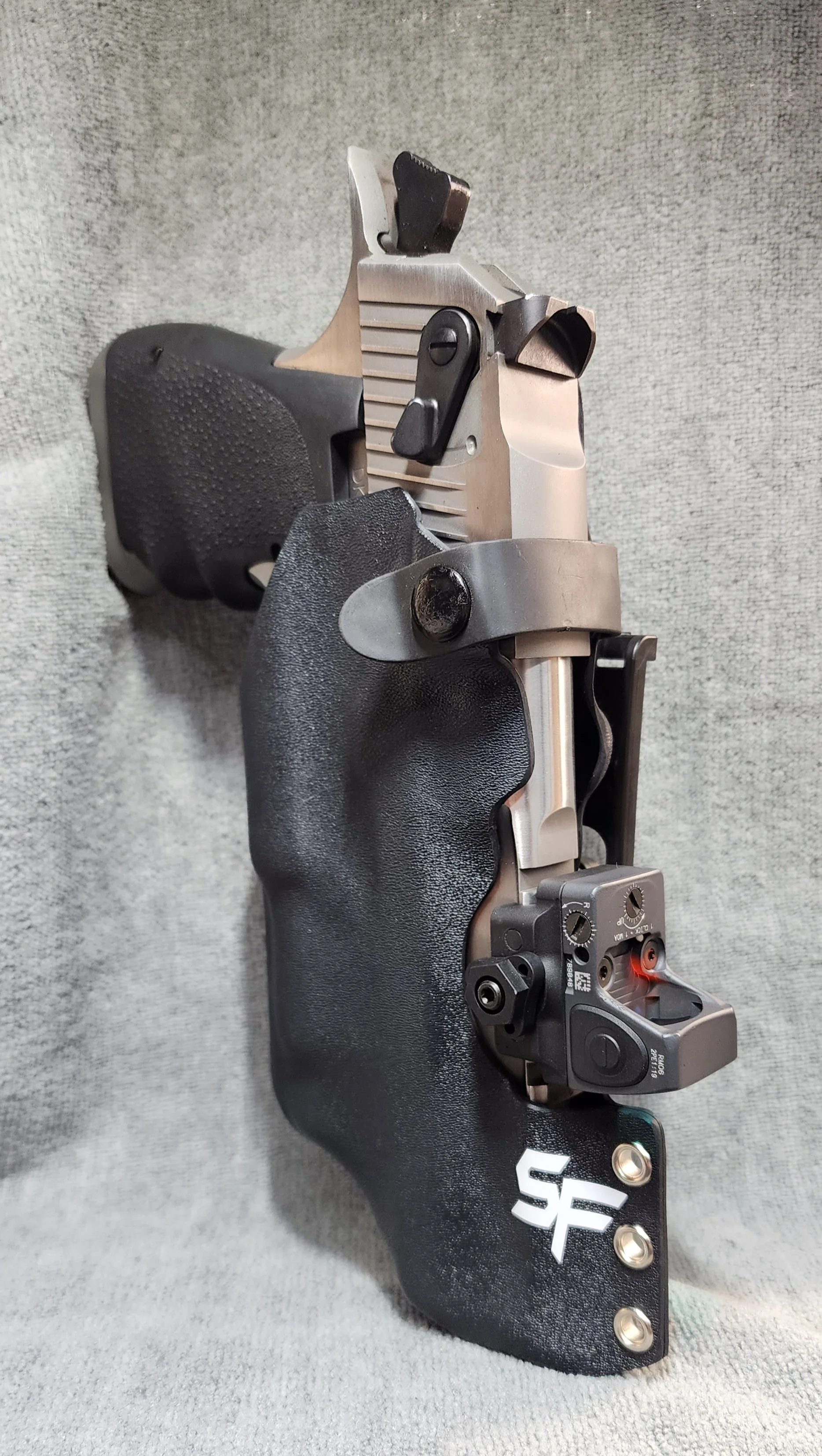 Close-up of a semi-automatic pistol with a black grip, mounted with a red dot sight, and fitted with a custom black grip extension.