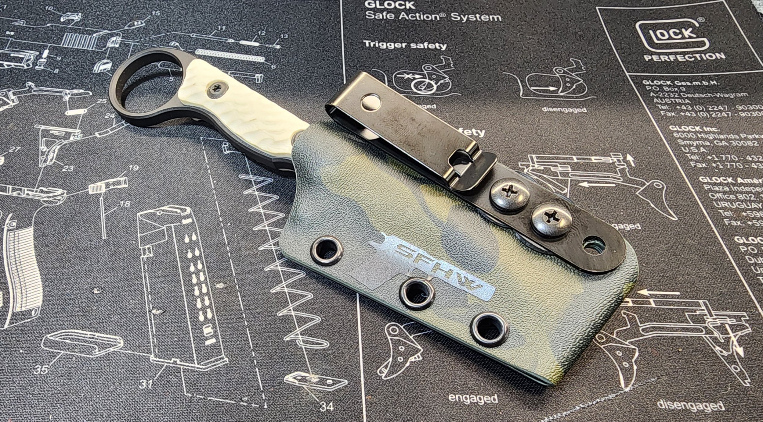 A firearm trigger mechanism with a spring, screws, and a grip on a gun maintenance mat with schematic diagrams.