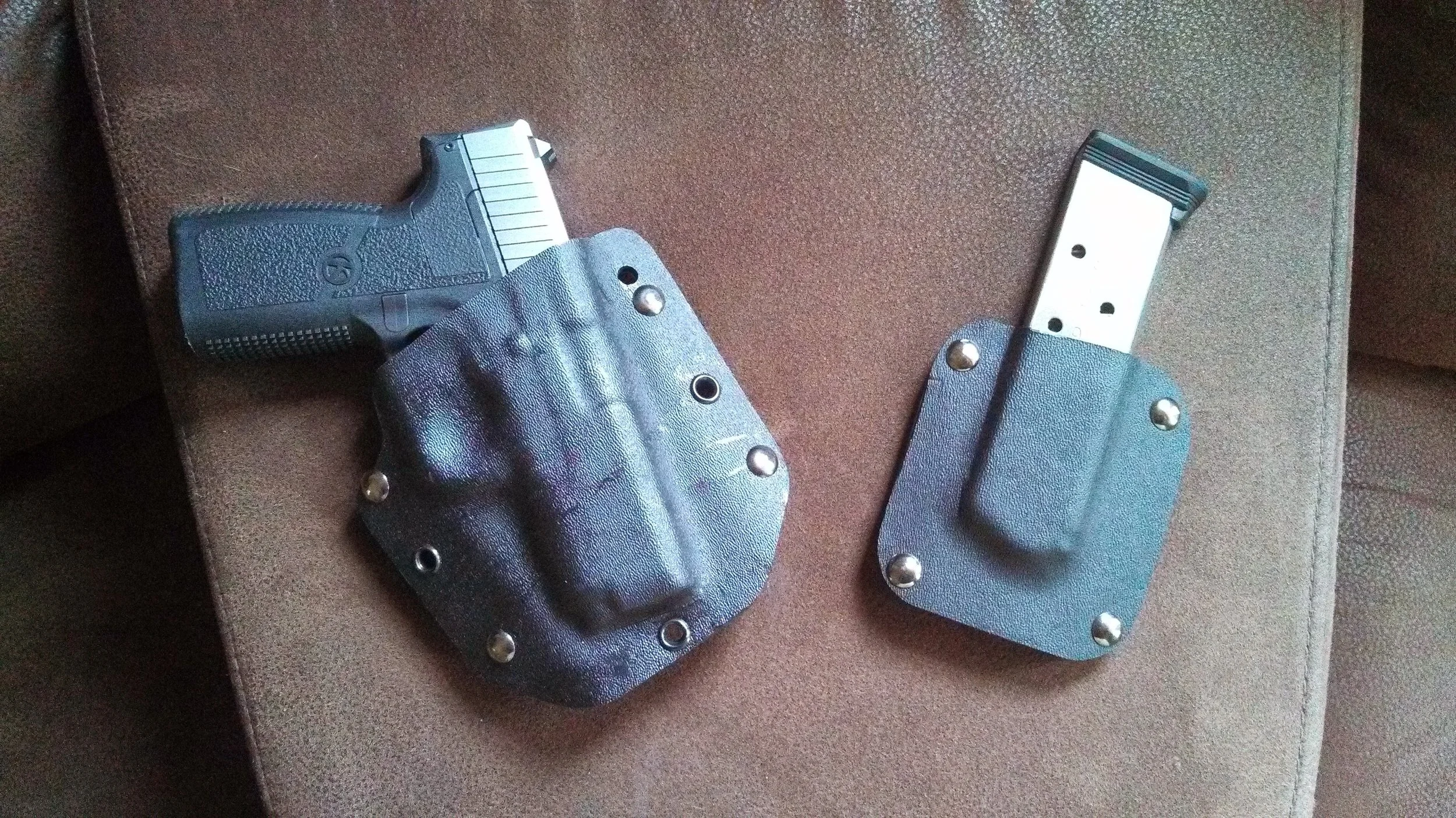 Handgun and magazine in black holsters on a brown fabric surface.