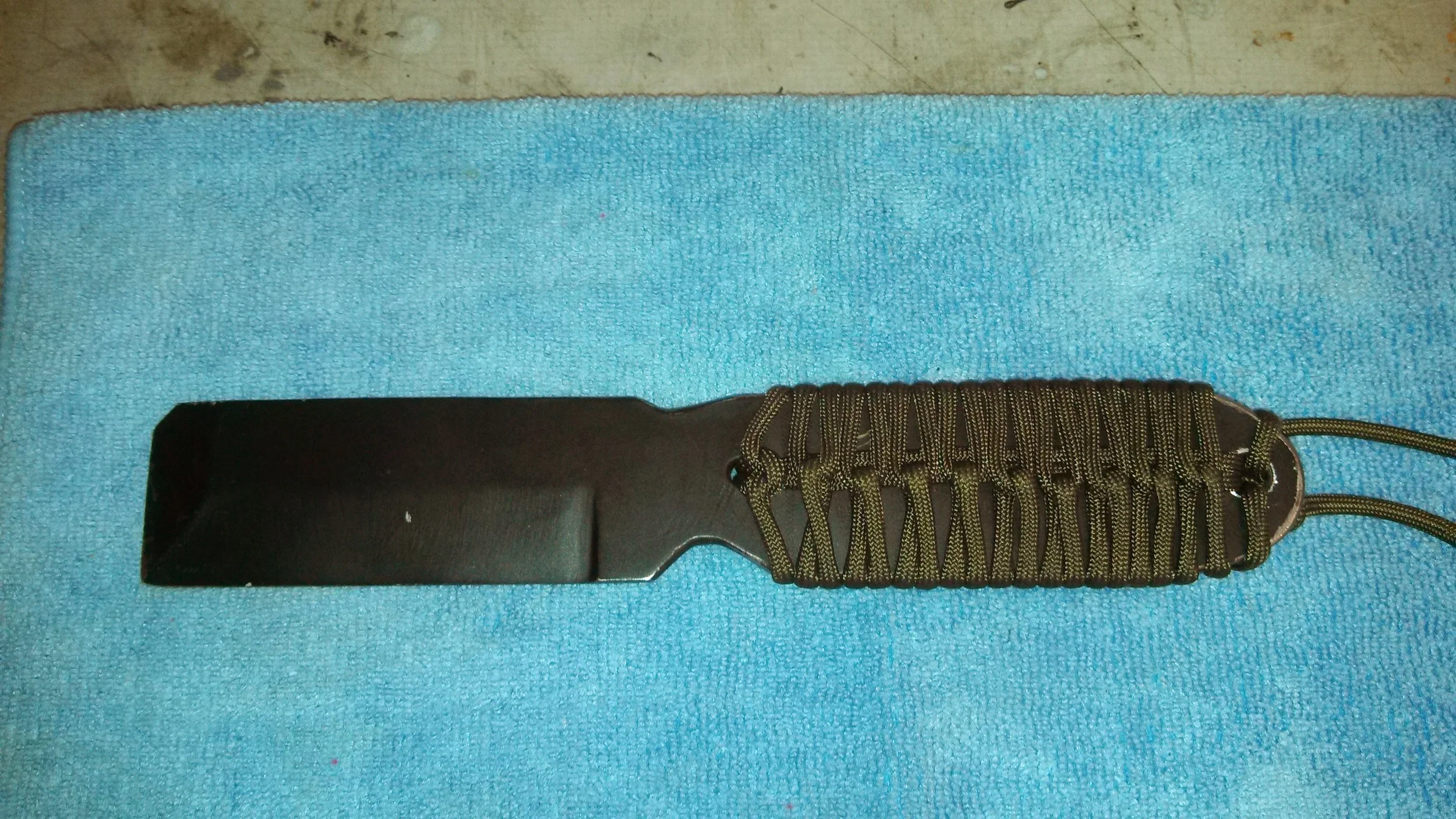 A black knife with a brown handle wrapped in green paracord, placed on a light blue towel.