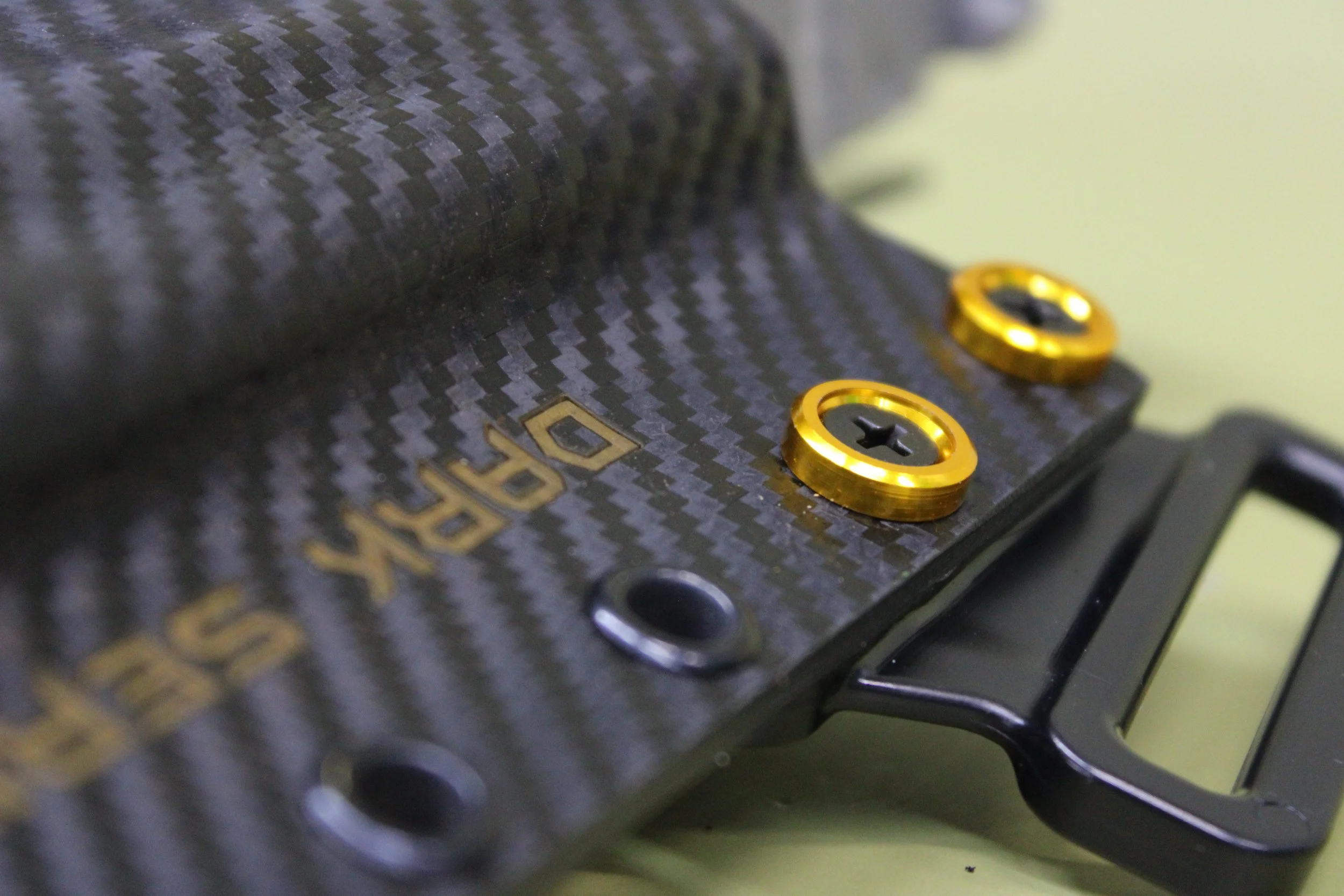 Close-up of a black carbon fiber camera rig with two gold-colored screws and gold lettering that says 'SB GEAR' on the surface.