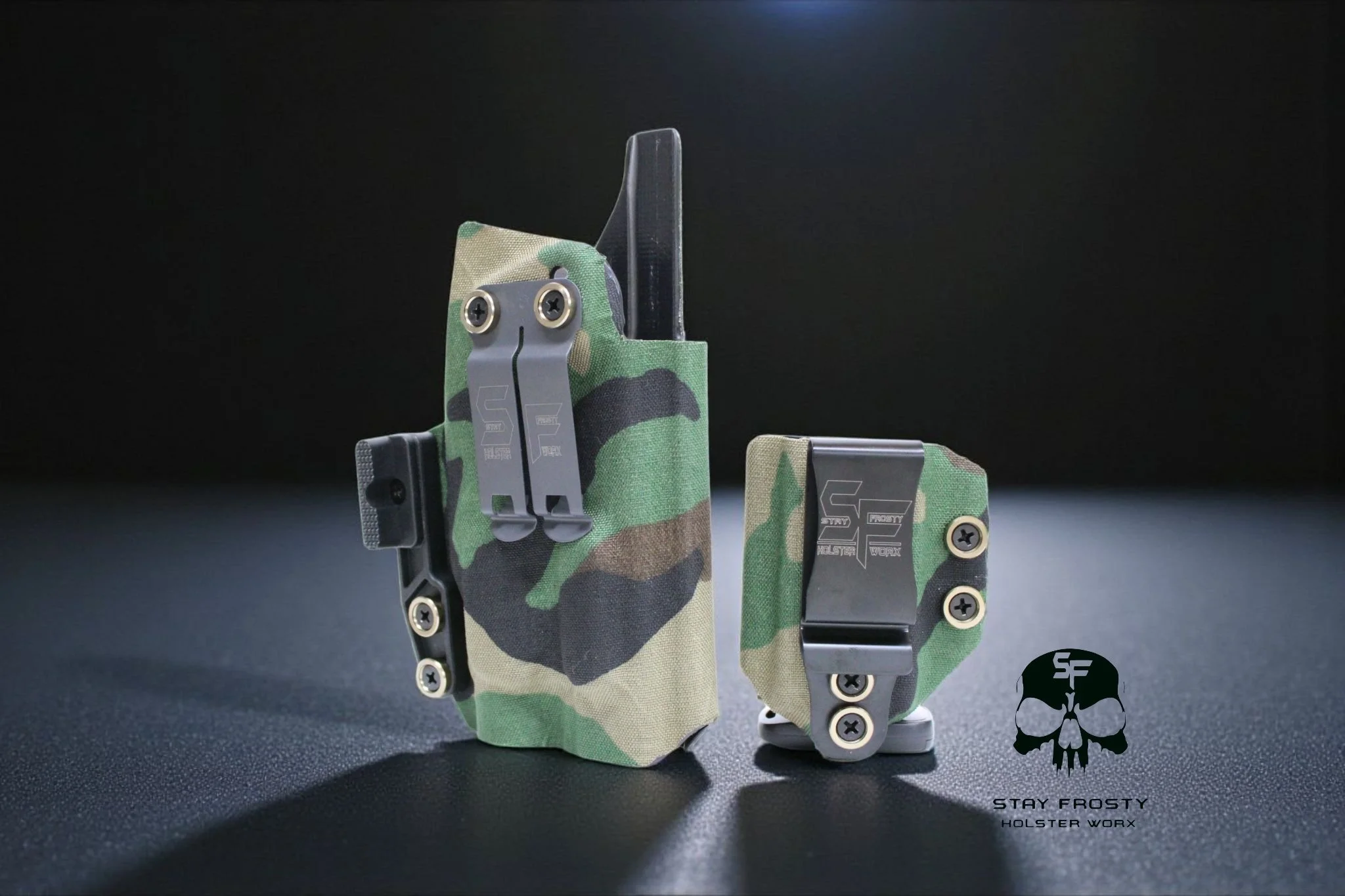 Two firearm holsters with camouflage fabric covers, metallic clips, and screws, placed on a dark textured surface against a black background, with a Stay Frosty Holster Worx logo in the bottom right corner.