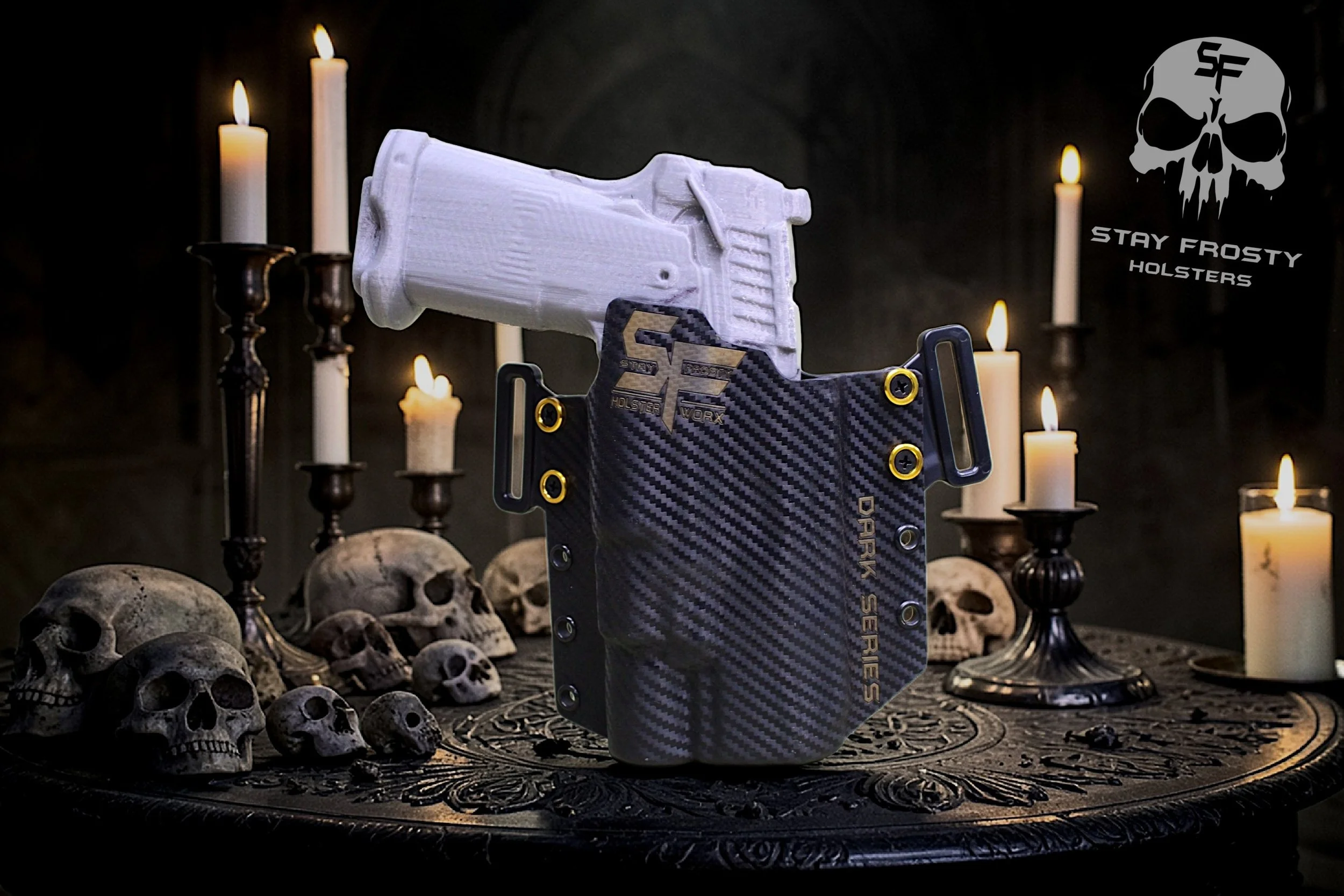 A black carbon fiber gun holster with gold accents and the logo 'SF' is placed on a gothic-style table surrounded by skulls and lit candles, with a 3D-printed white gun in the background and a logo reading 'Stay Frosty Holsters' in the upper right corner.