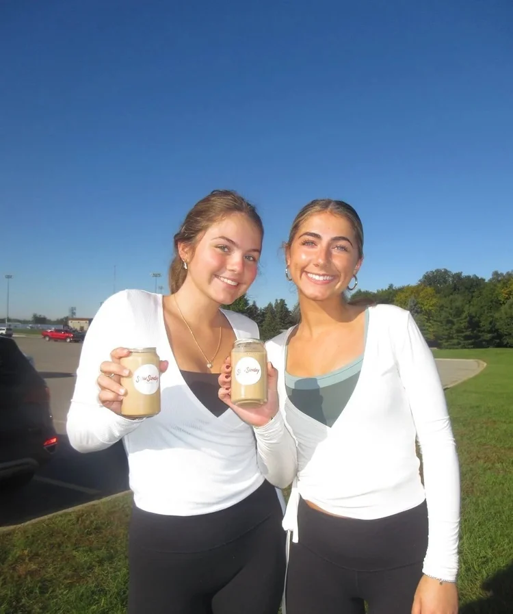Two women holding iced coffees from Slow Sunday outdoors at a party