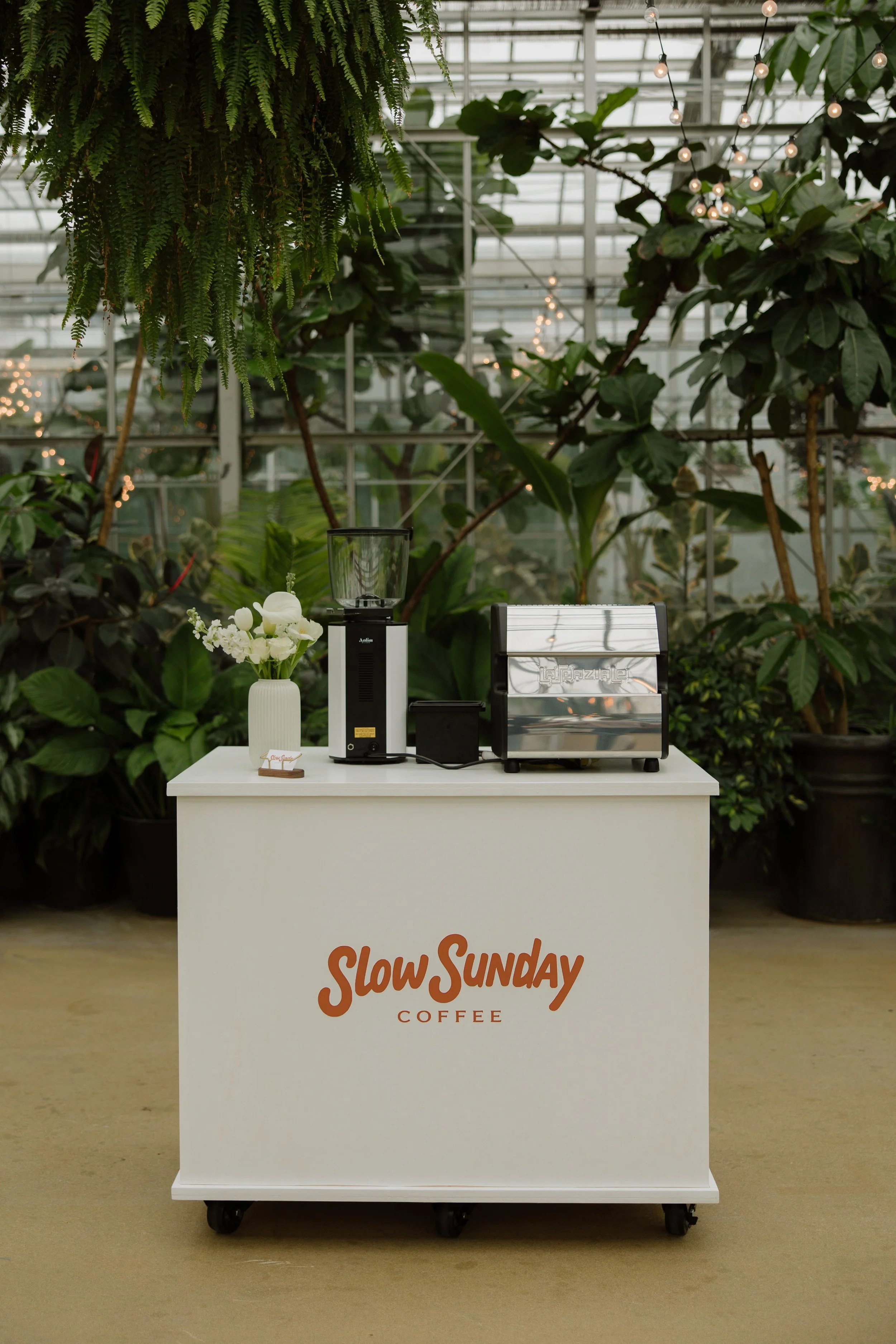 A white coffee stand with orange text that says "Slow Sunday Coffee" on the front