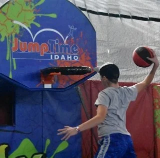 A boy playing basketball at Jump Time IDAHO game center, aiming to shoot a ball into the hoop.