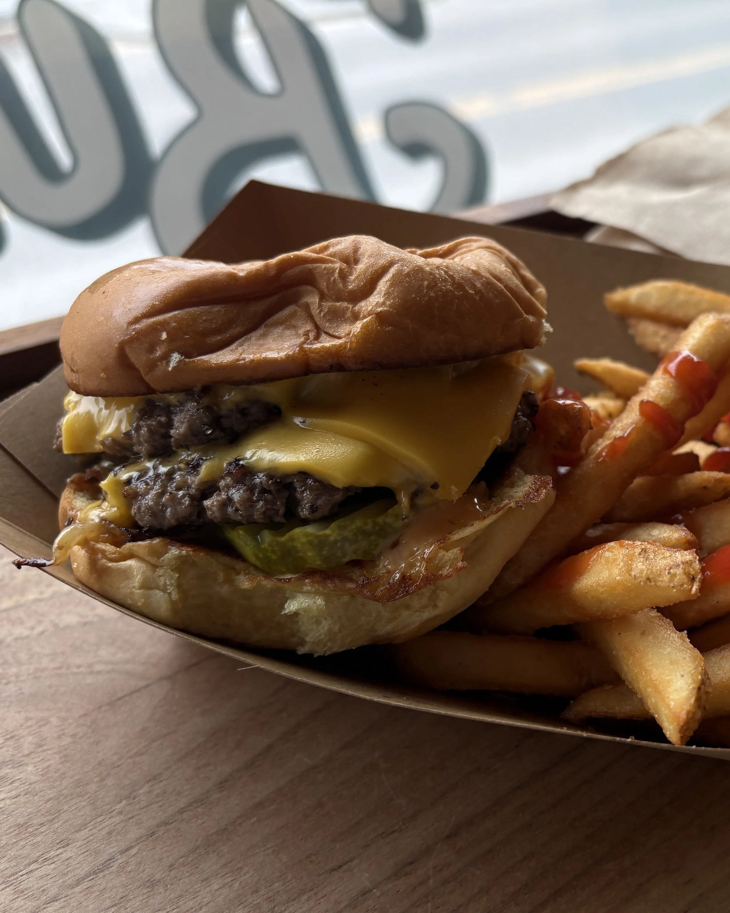 Close-up of a cheeseburger with a beef patty, melted cheese, lettuce, and a bun, served with seasoned French fries on a tray.