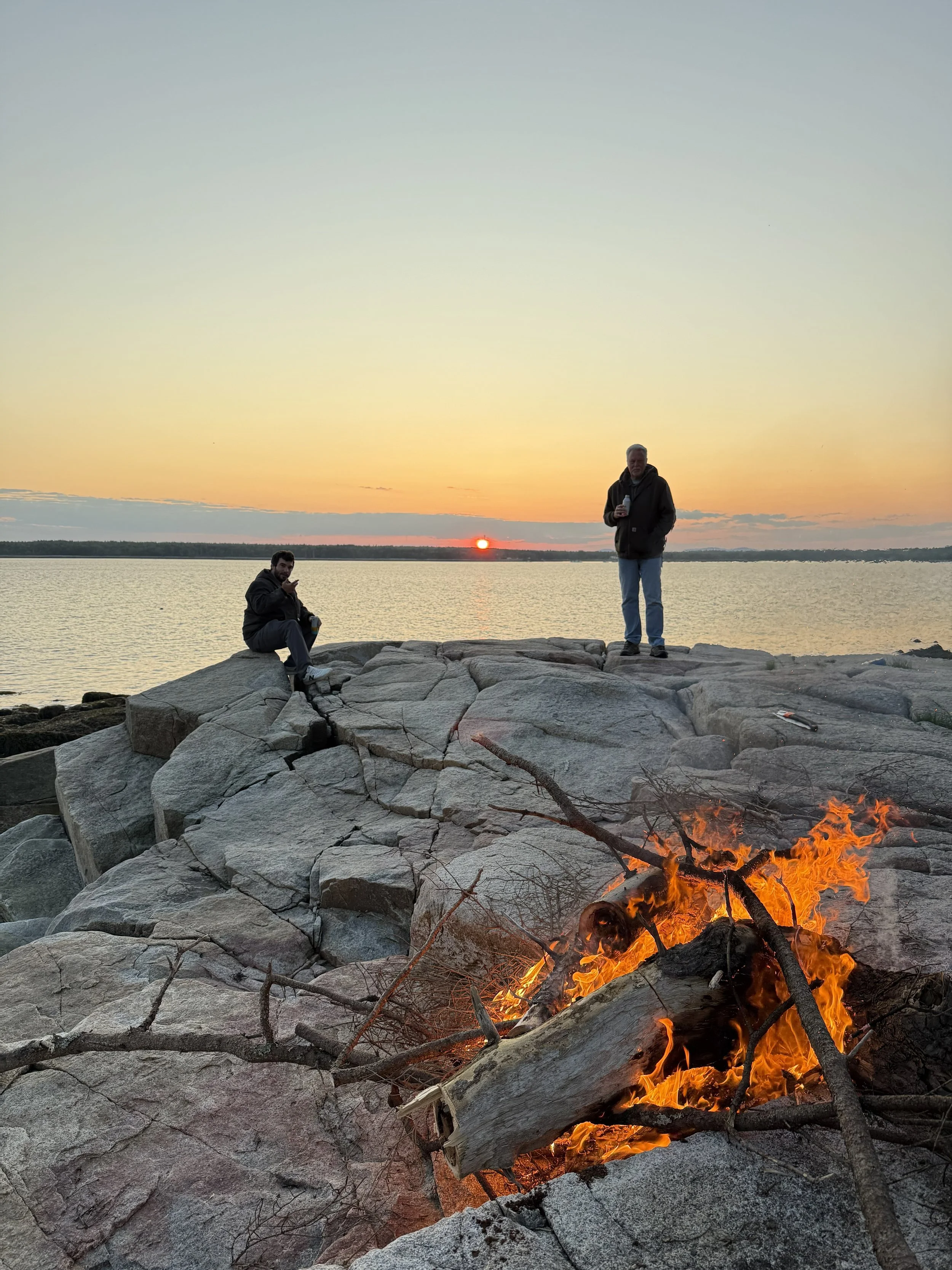 Adventure motorcycle riders enjoying a fire pit in Downeast Maine during a guided Northbound Moto tour