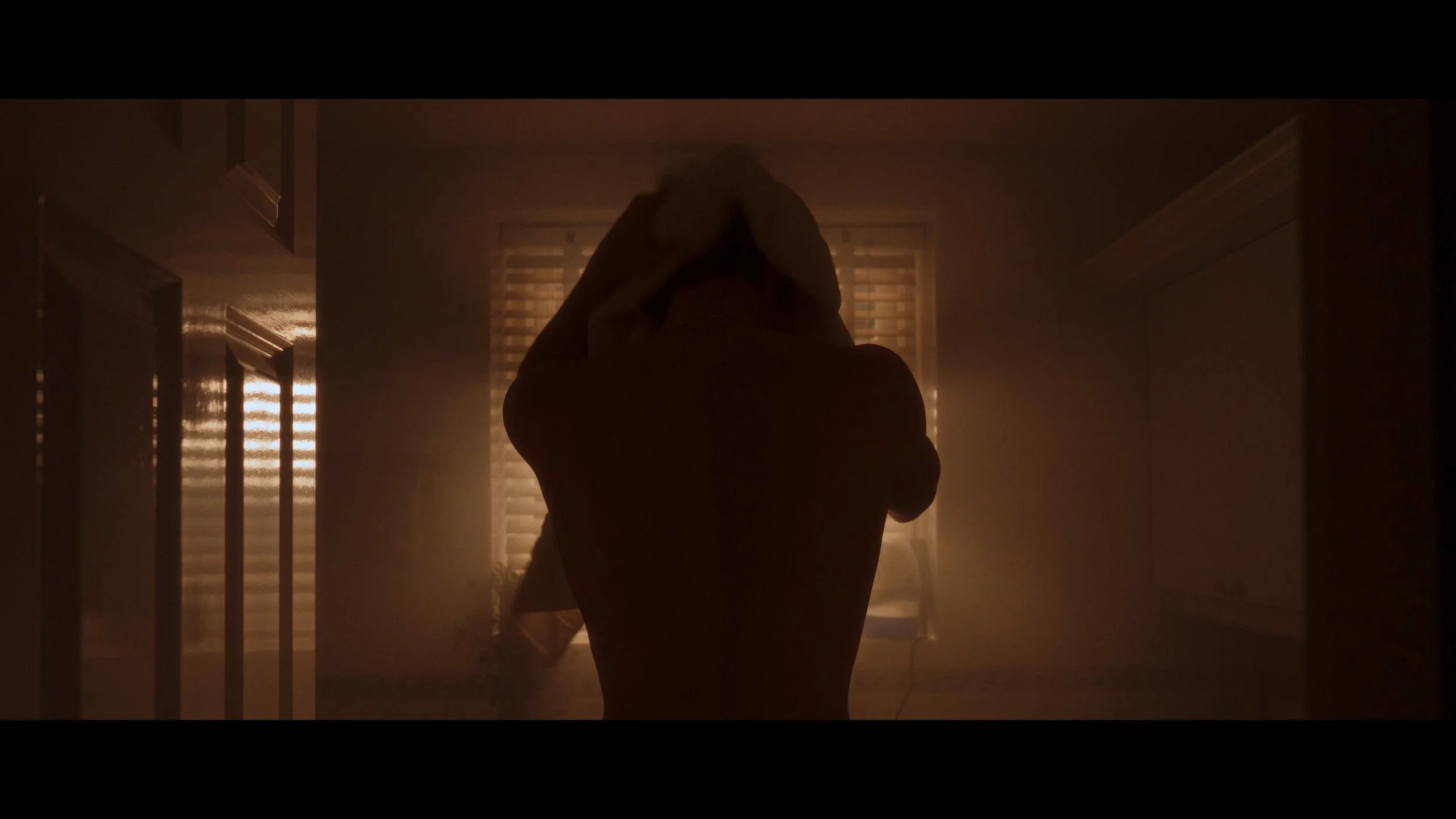 A silhouette of two people embracing in a dimly lit room with warm light coming through closed blinds.