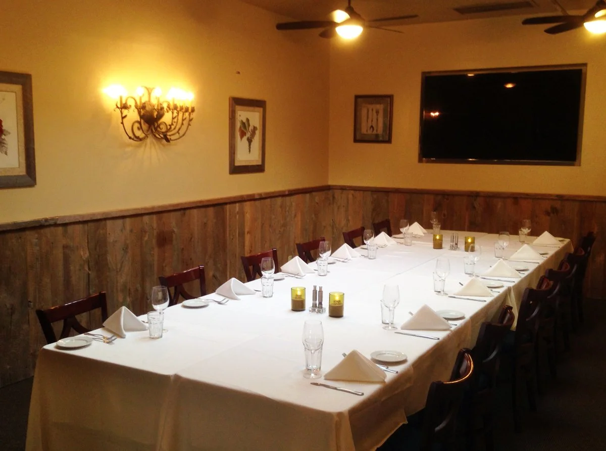 Image of a room with wooden sideboards and a long table set with table cloths. Thoughtfully decorated and ready for a gathering.