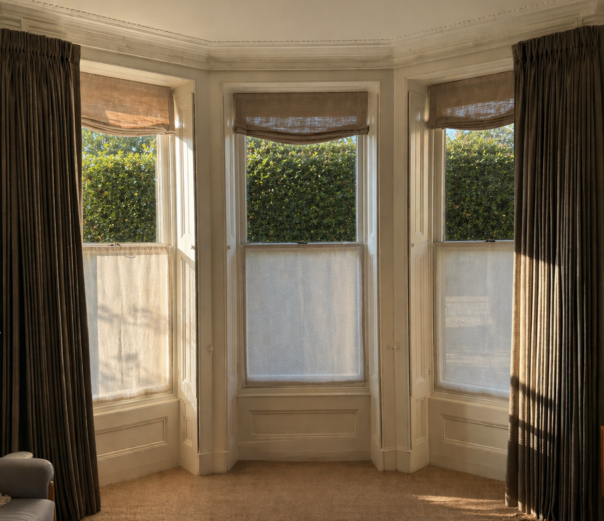 Bay window dressed in linen café curtains, and sheer relaxed roman blinds. Framed with triple pinch pleat, full length drapery
