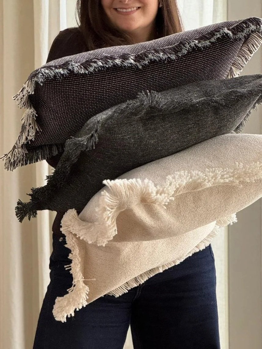 A woman holding four decorative throw pillows of different colors and textures, arranged from dark to light.