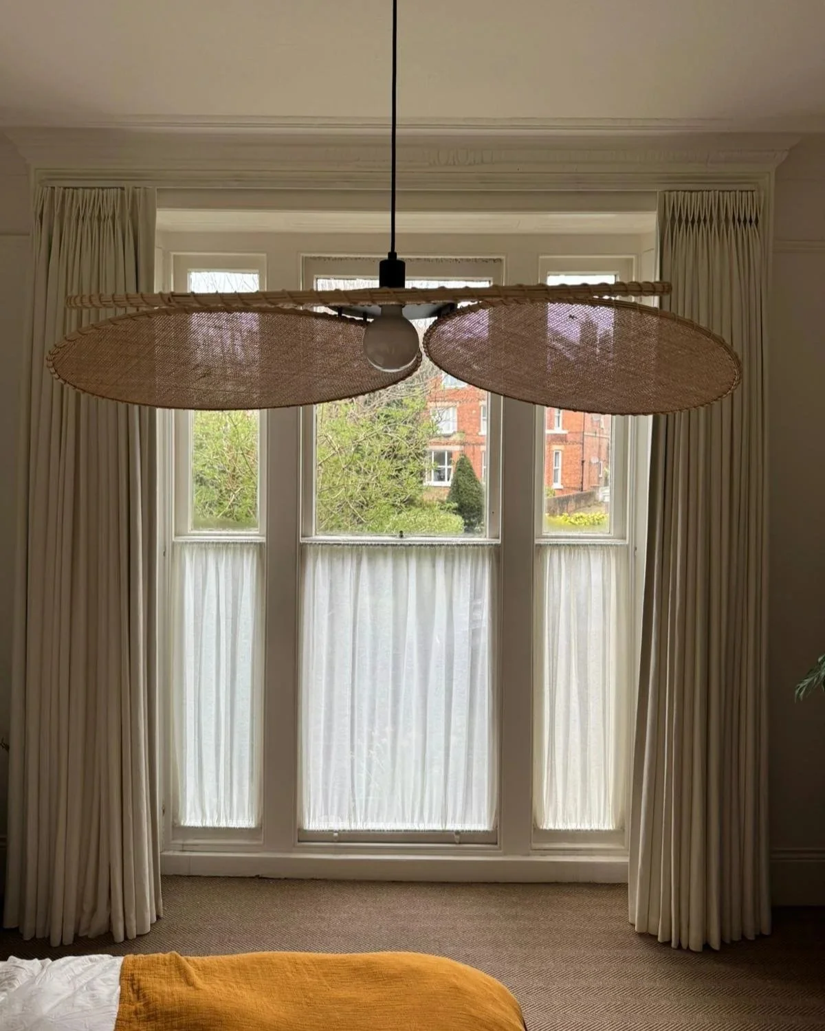 View of a room with large windowed doors, beige curtains, and a modern hanging light fixture.