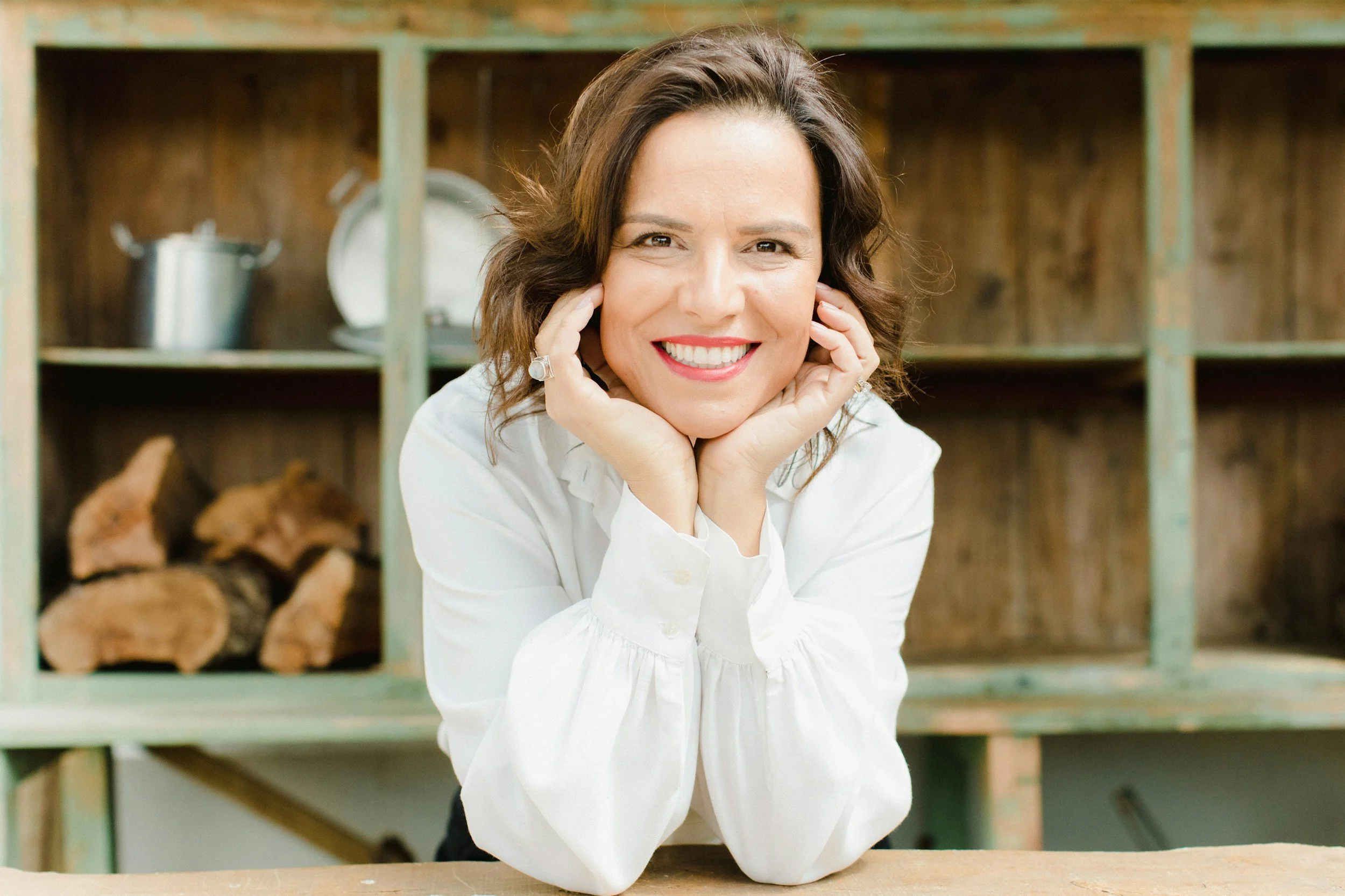 woman smiling while resting her elbows on a table with her hands framing her face