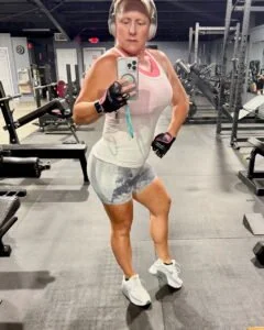 Woman taking a mirror selfie at the gym, wearing workout clothes and headphones.