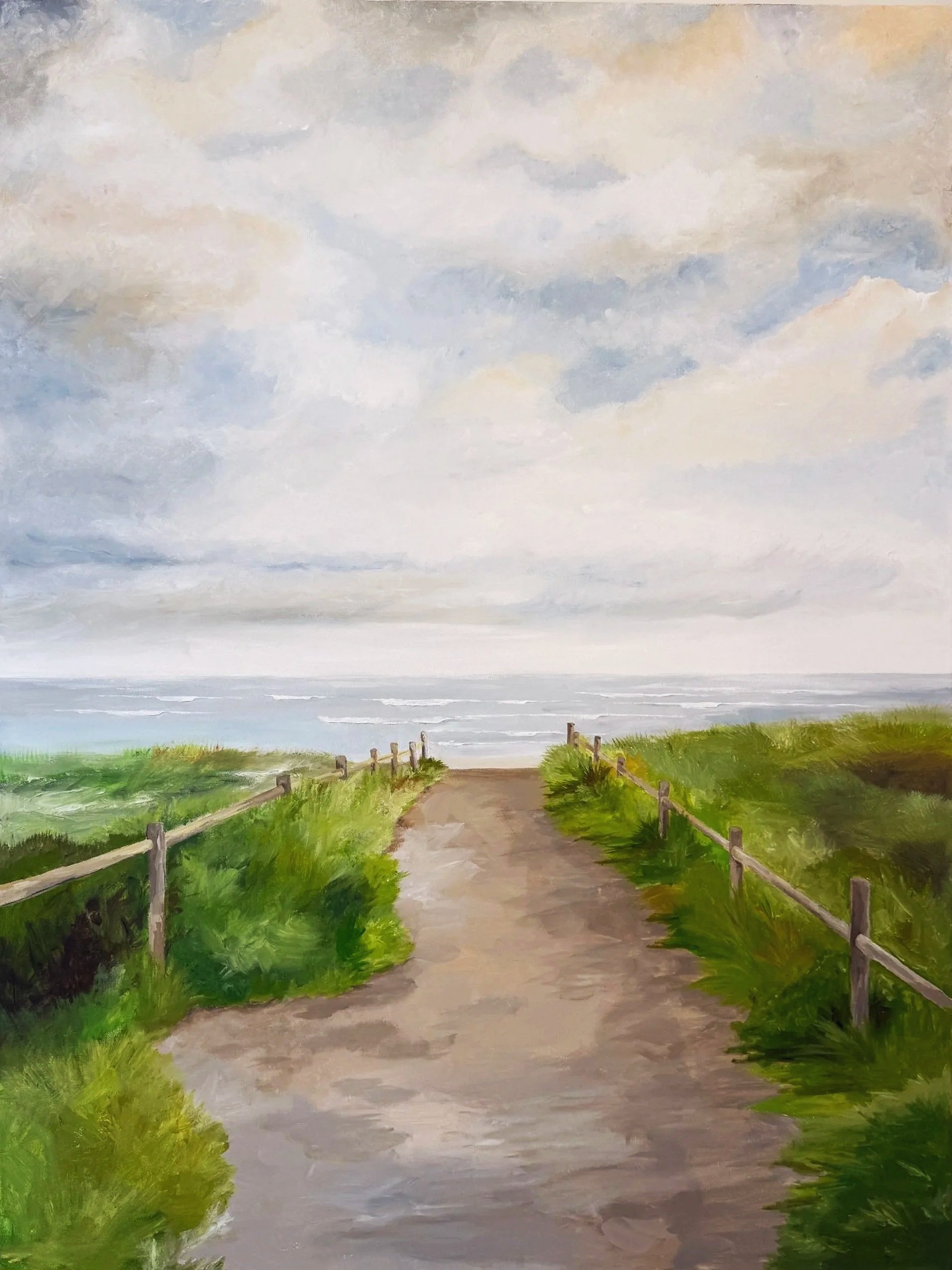 Painted beach pathway with green grass on both sides, wooden fence, cloudy sky, and ocean in the distance.