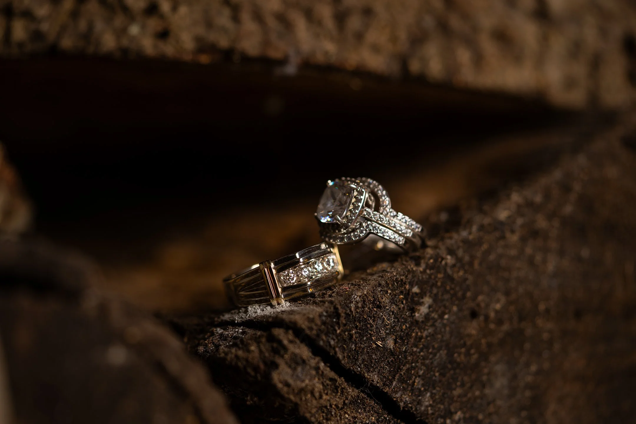 Two silver rings with diamonds resting on a rough, brown wooden surface.