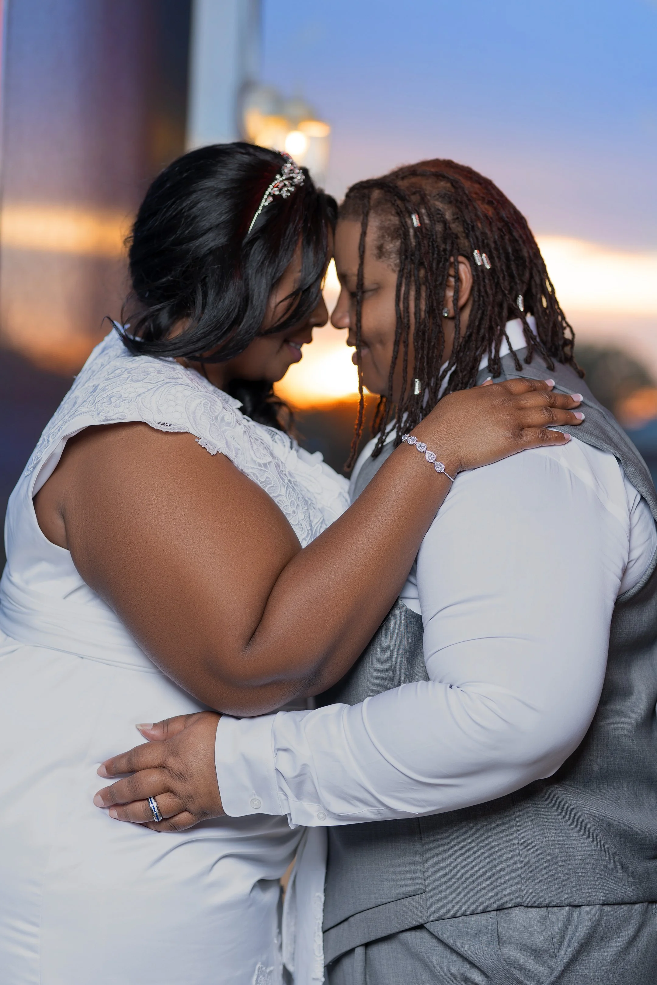 A couple dressed in wedding attire sharing an intimate moment outdoors at sunset.