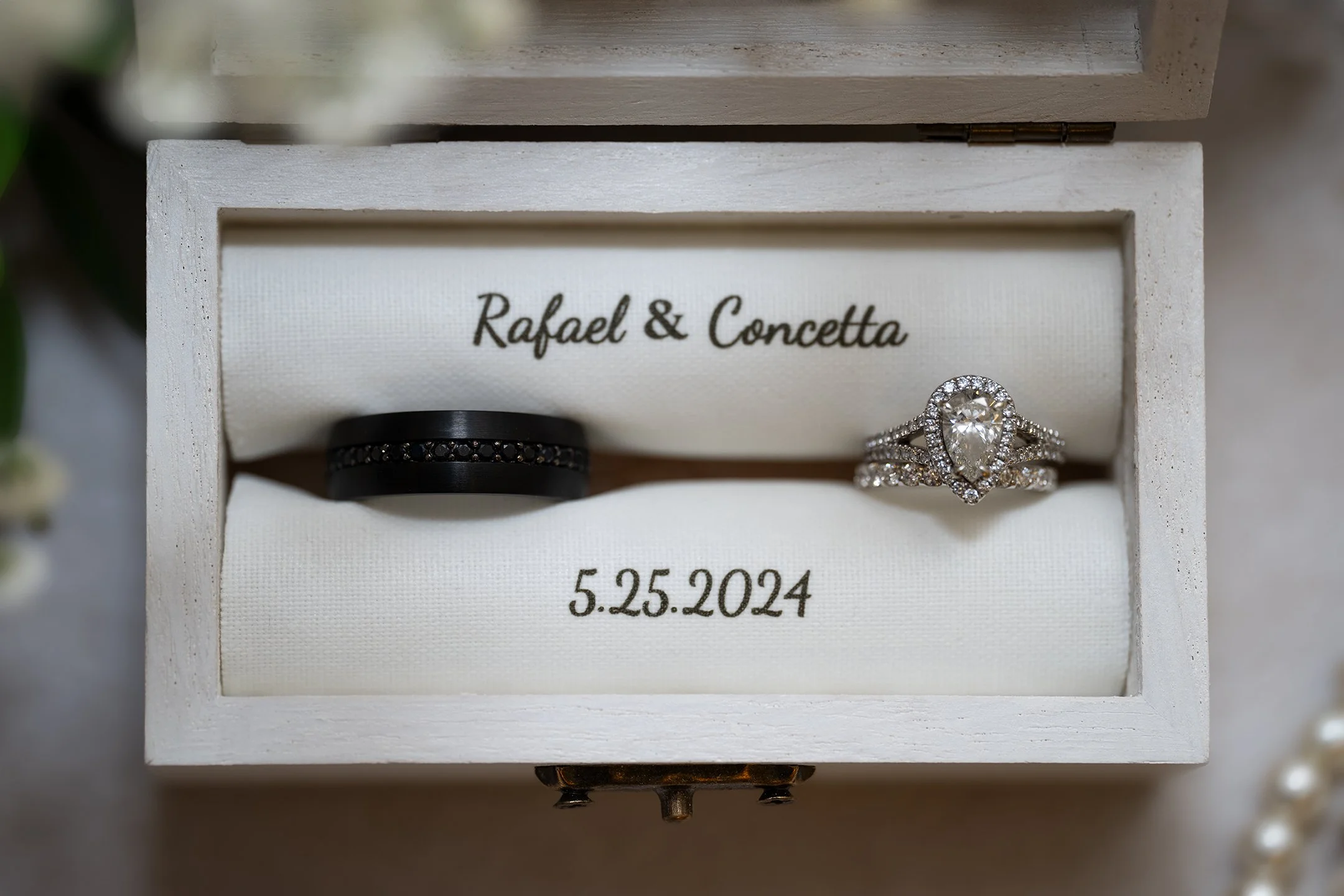 Wedding rings in a white box with the names Rafael and Concetta and the date 5.25.2024 written inside.