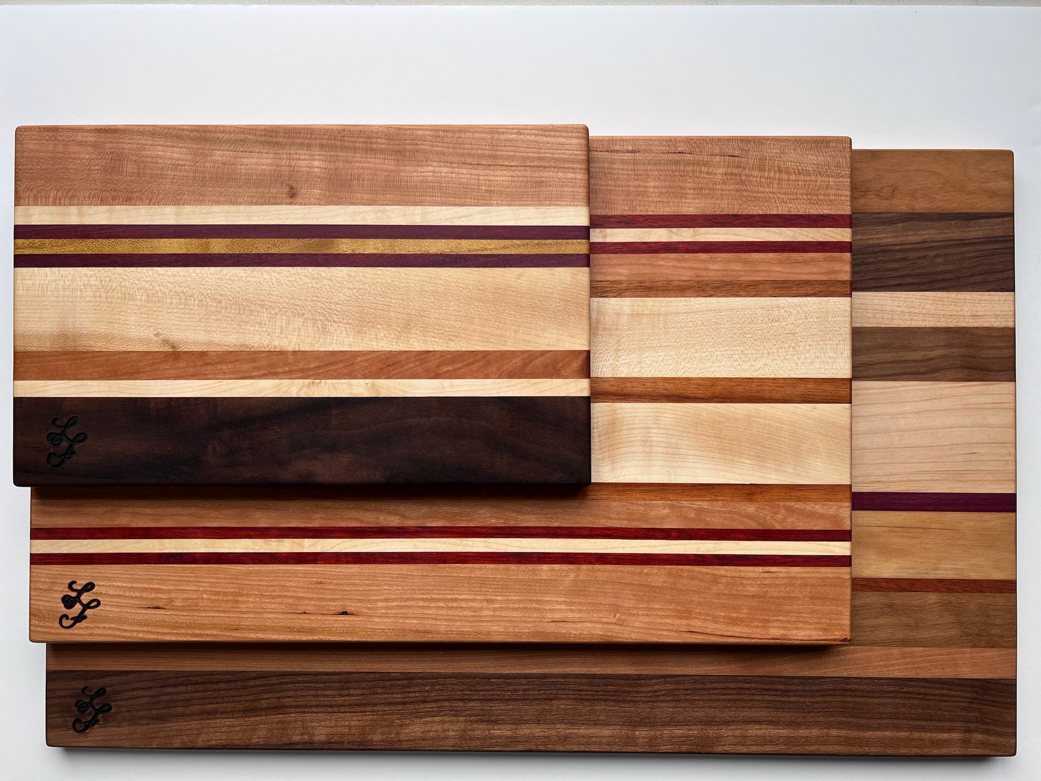 Several wooden cutting boards with various wood tones and stripe patterns stacked on top of each other.
