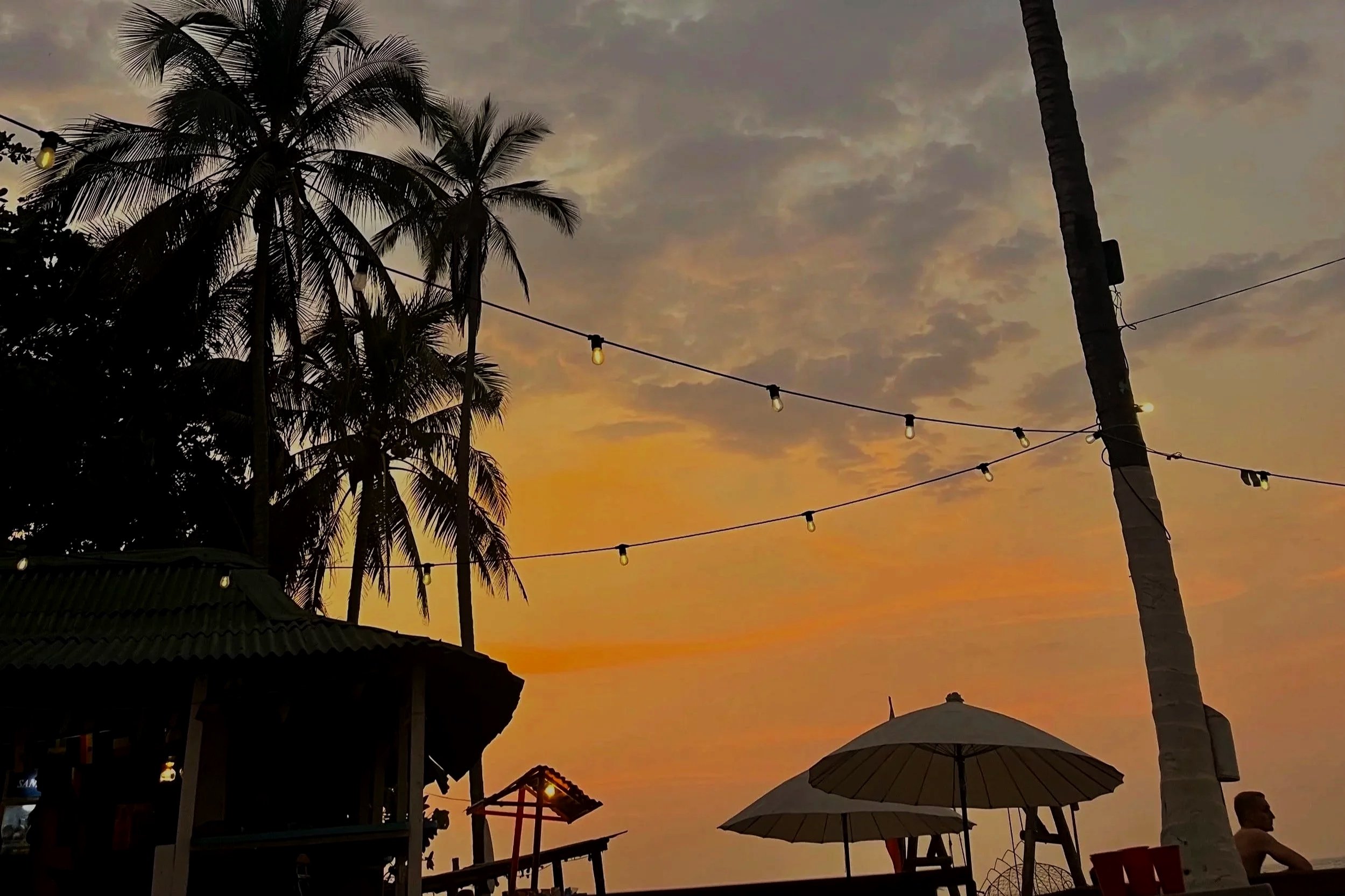 Coucher de soleil tropical avec silhouettes de palmiers, parasols et guirlandes lumineuses