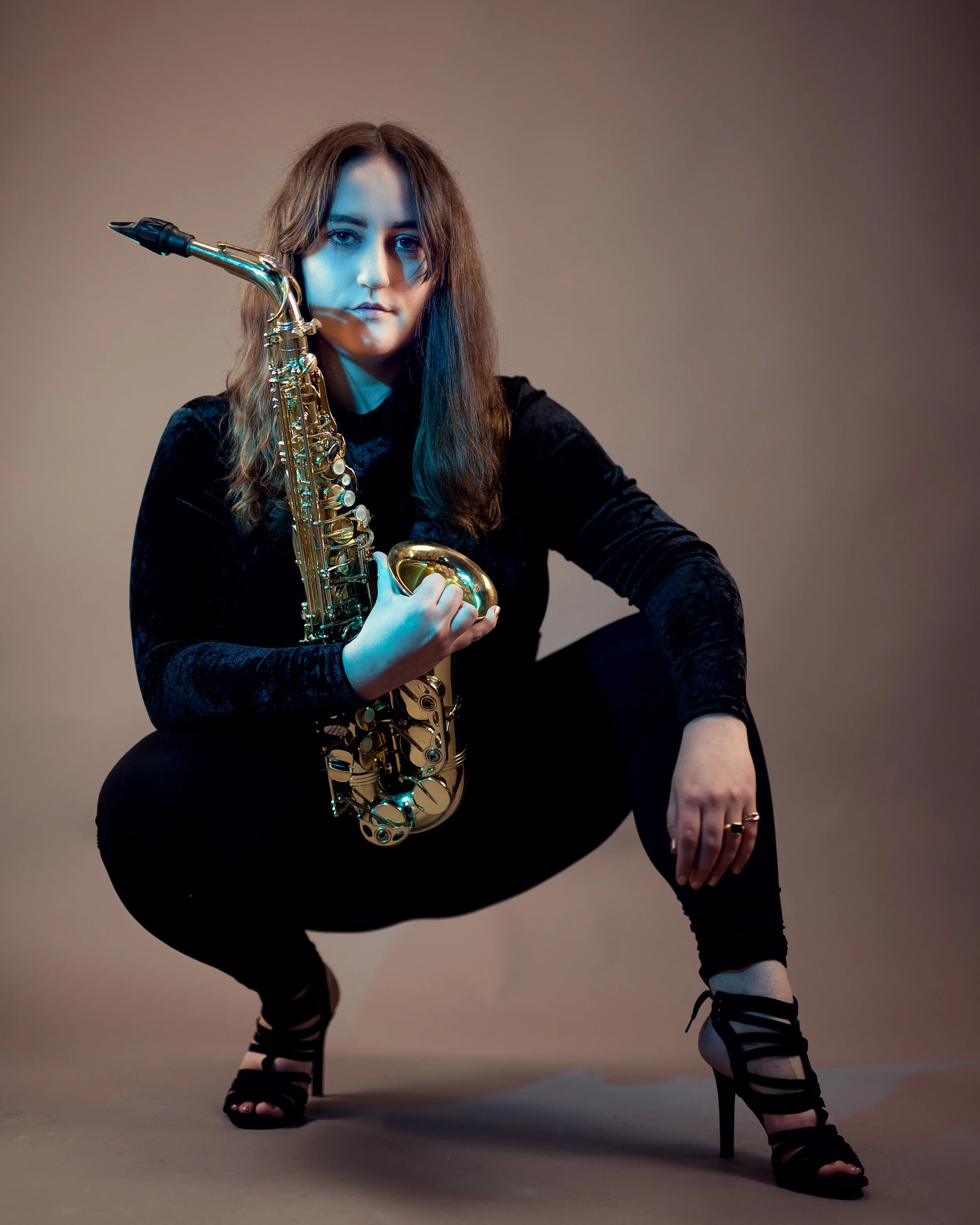 Die Künstlerin Pascale Feiertag hockend in einem komplett schwarzen Outfit mit einem Altsaxophon in der Hand