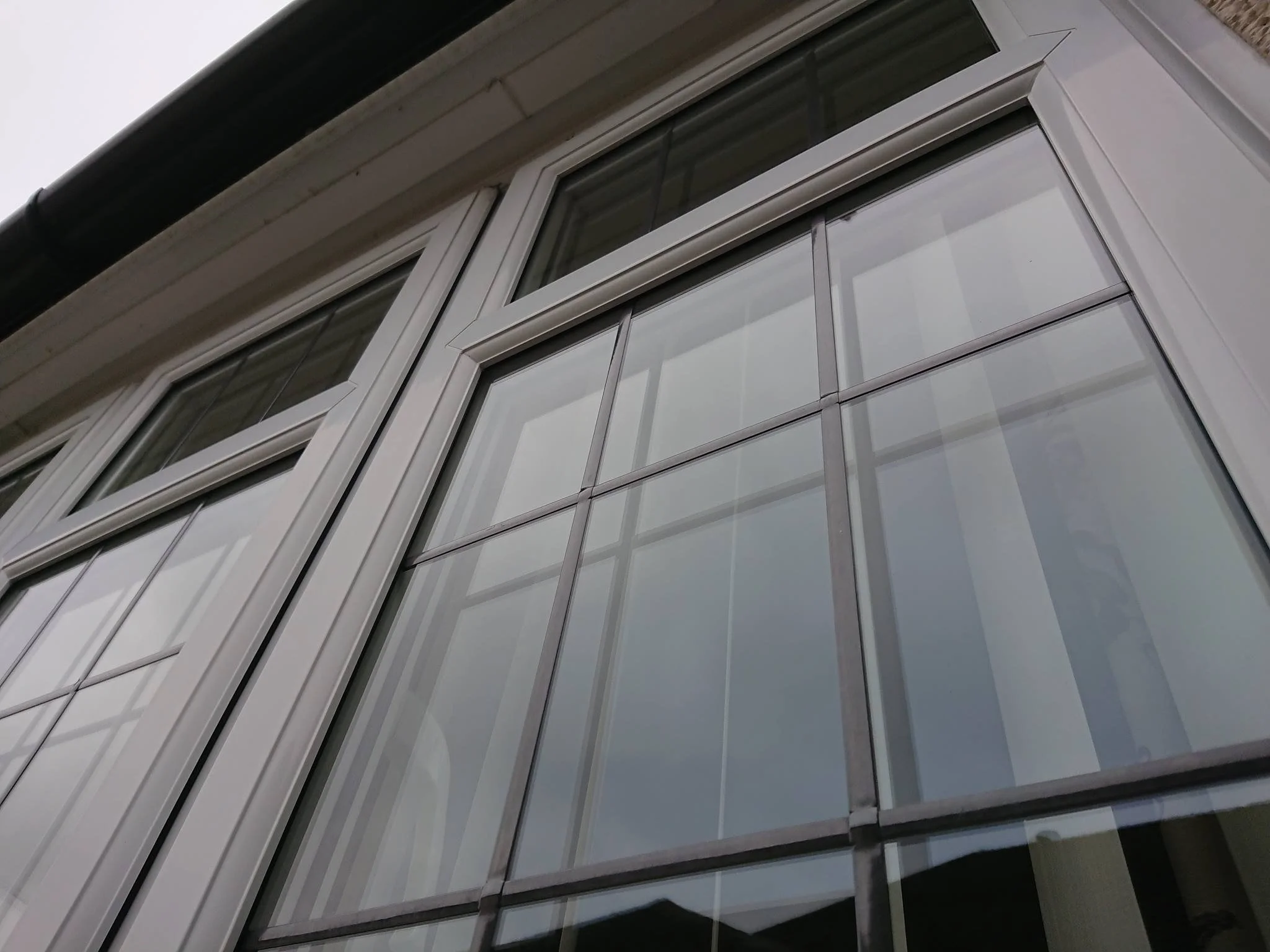 Close-up of a modern house window with a white frames and glass panes, reflecting a cloudy sky.