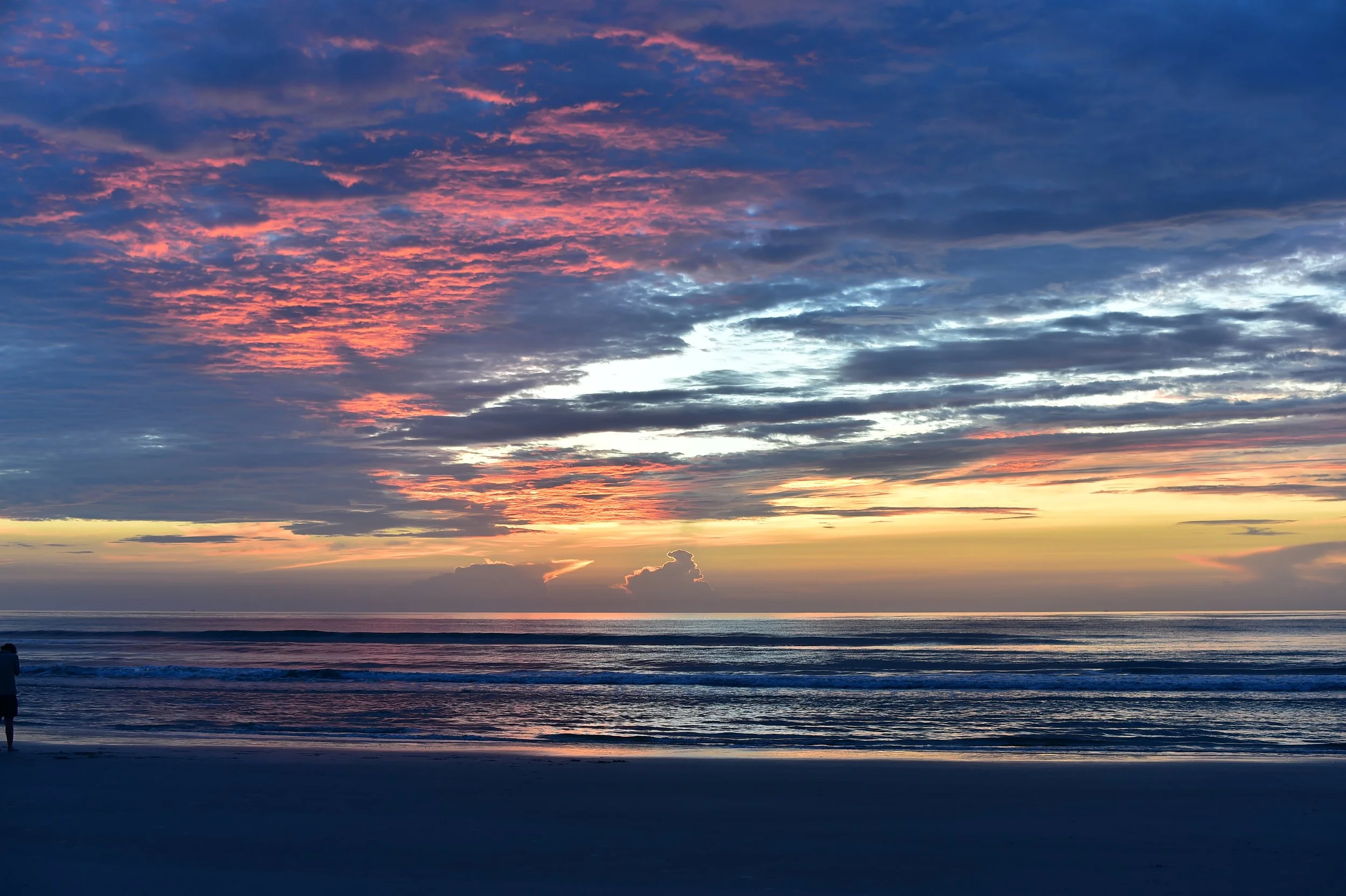 Sunset over the ocean with colorful clouds in shades of pink, orange, and purple, and a calm sea reflecting the sky.