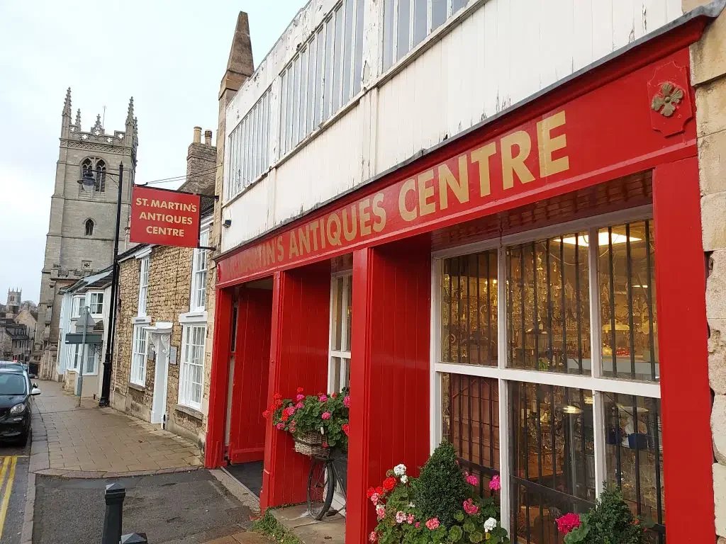 Exterior view of St. Martin's Antiques Centre with a red storefront, large windows, and potted plants.