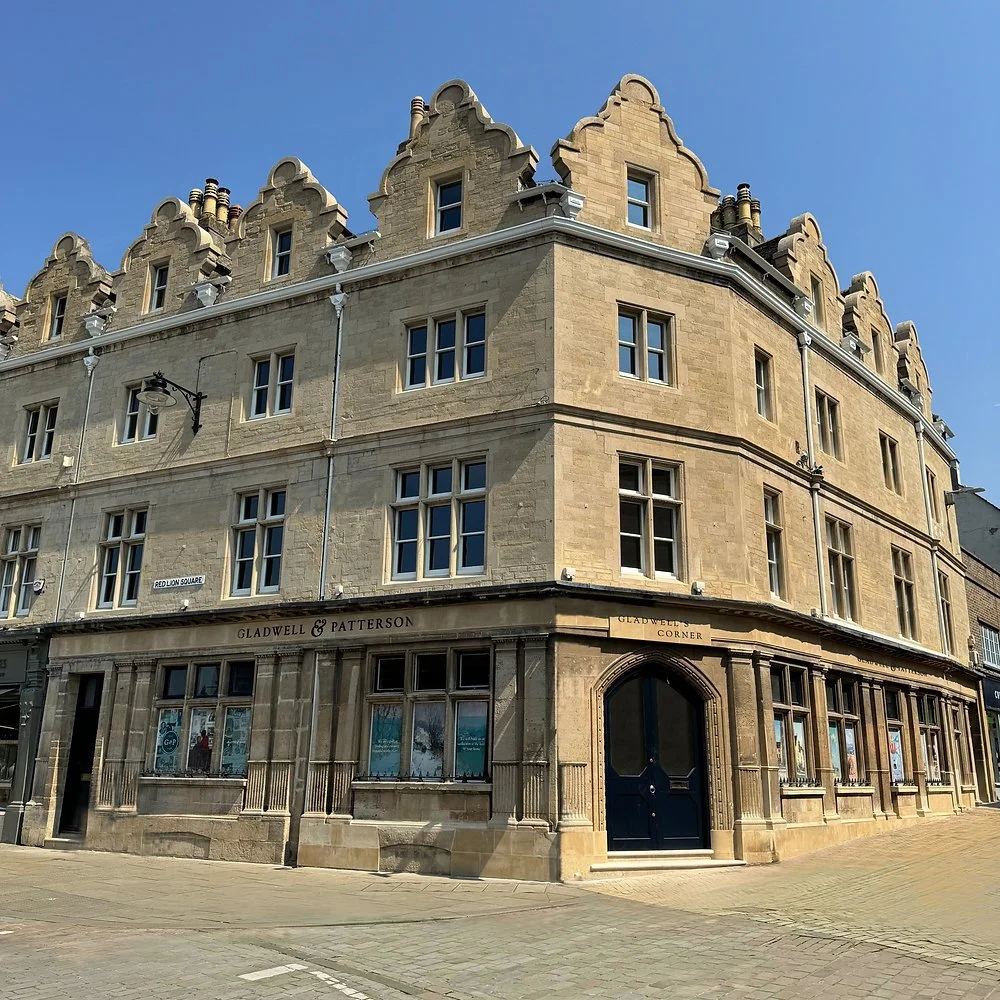 A historic corner building with stone architecture, multiple windows, and a sign reading 'Gladwell & Patterson' at the ground level, located at the intersection of Red Lion Square.