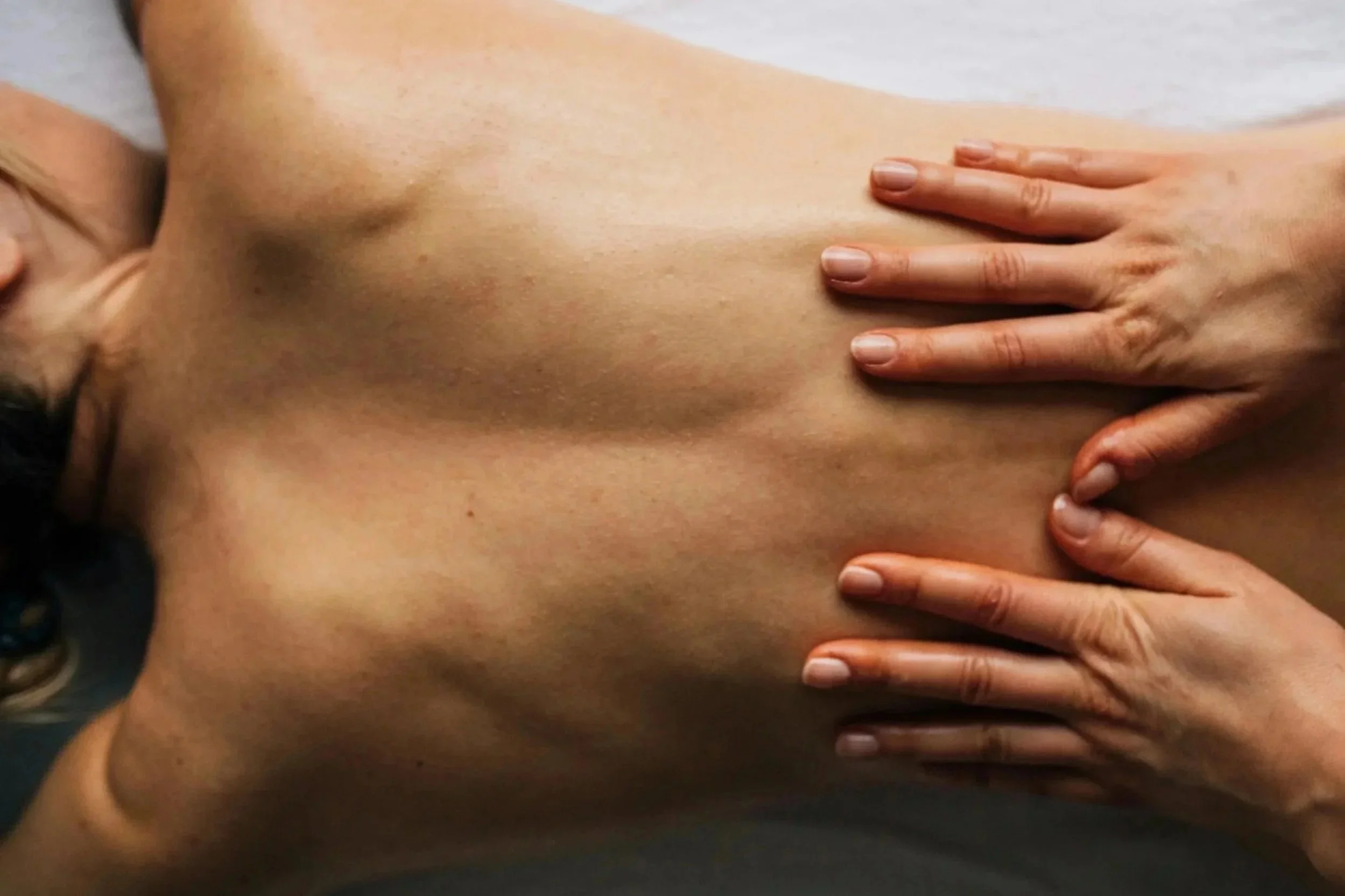 Close-up of a person's bare back being massaged with hands.